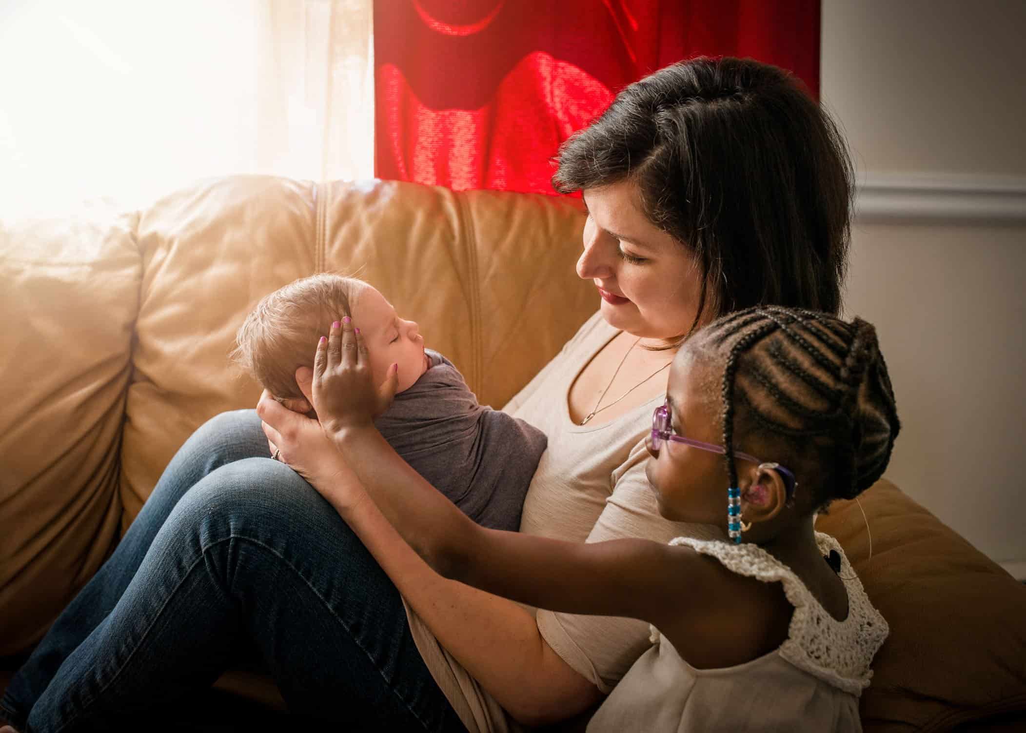 Mom holding her newborn son while her adopted daughter pats him gently