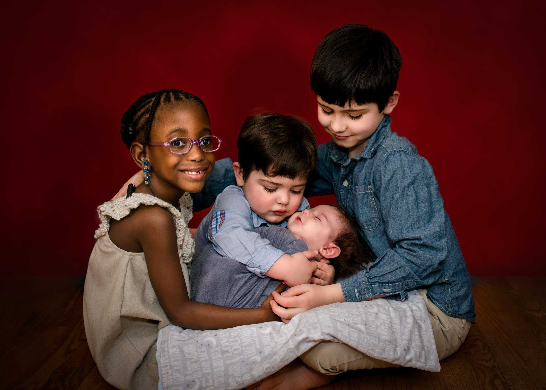 three siblings holding newborn baby in their laps