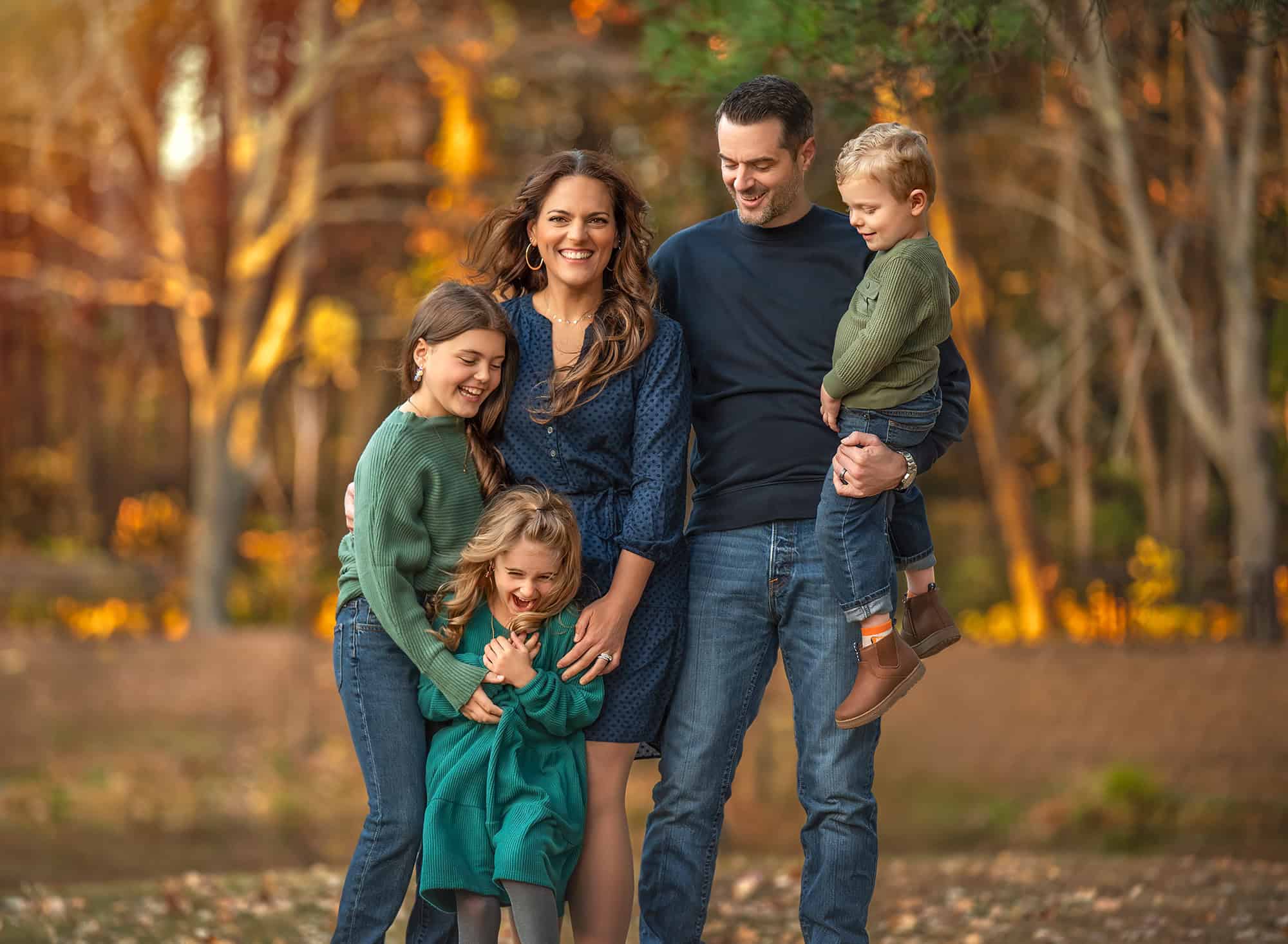 Parents standing with three children in warm evening light, autumn trees behind them.