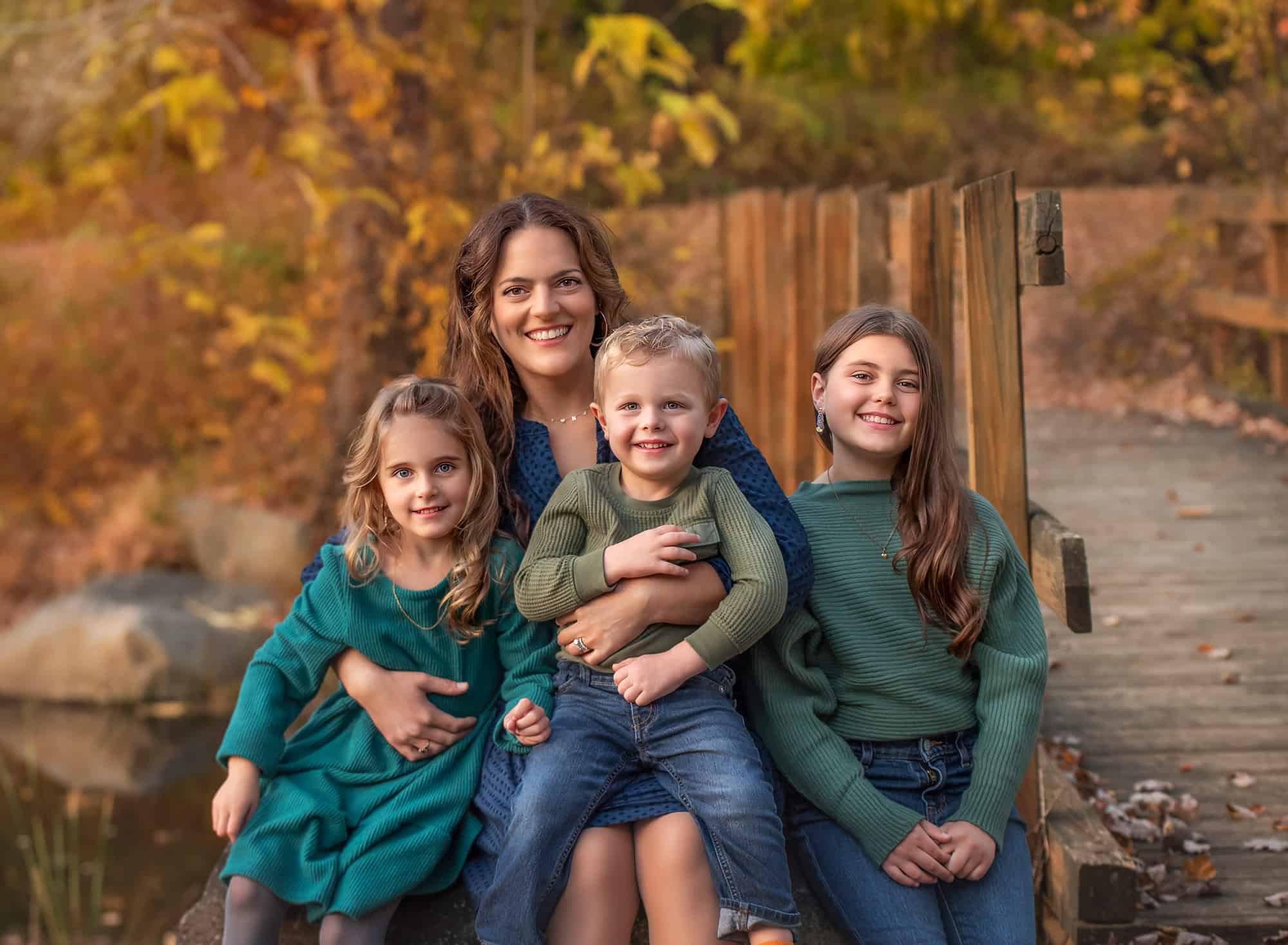 Mother with three children sitting along a wooden bridge, golden leaves surrounding them.