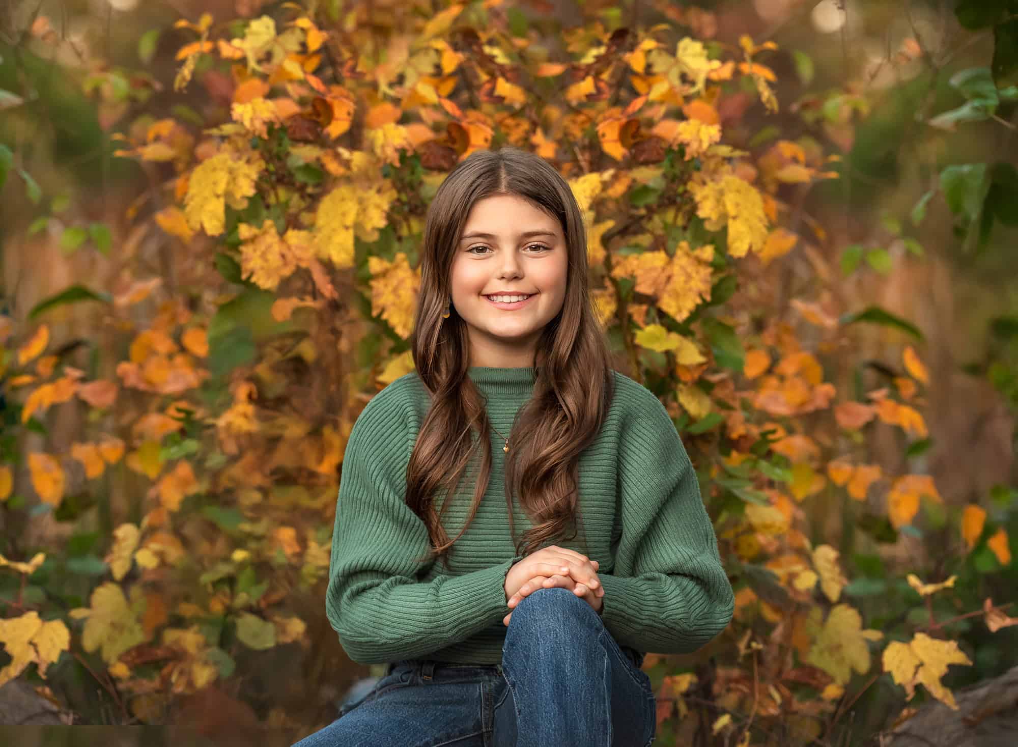 Portrait of the oldest daughter seated in front of yellow and green leaves, soft autumn light.