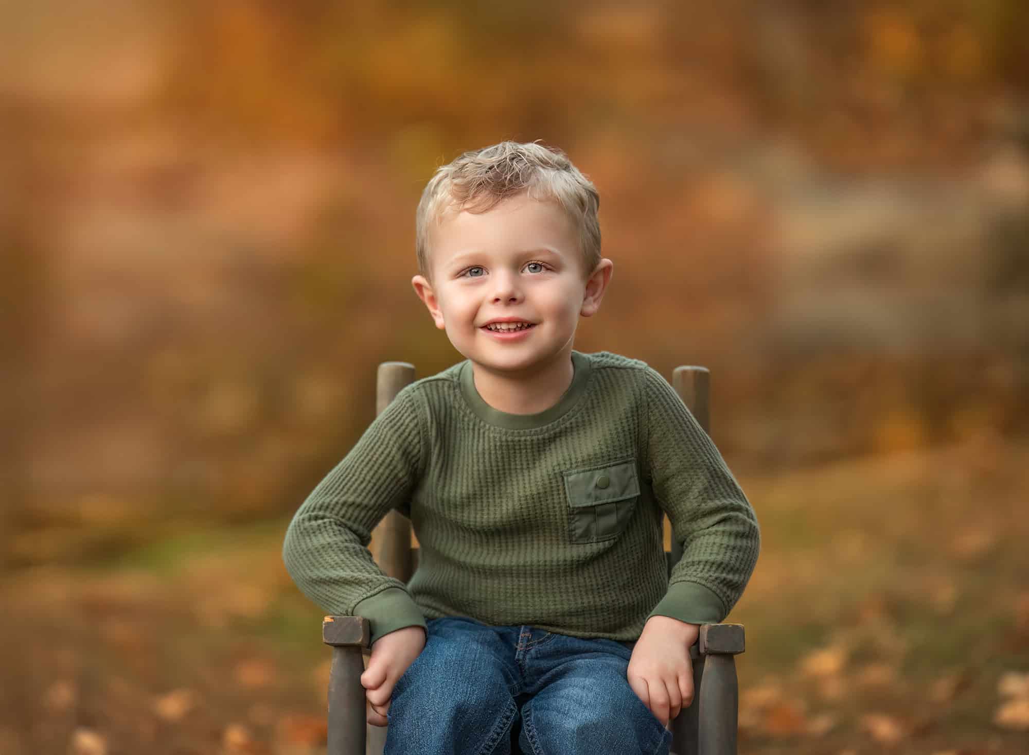 Portrait of the toddler son on a small chair, warm fall tones behind him.
