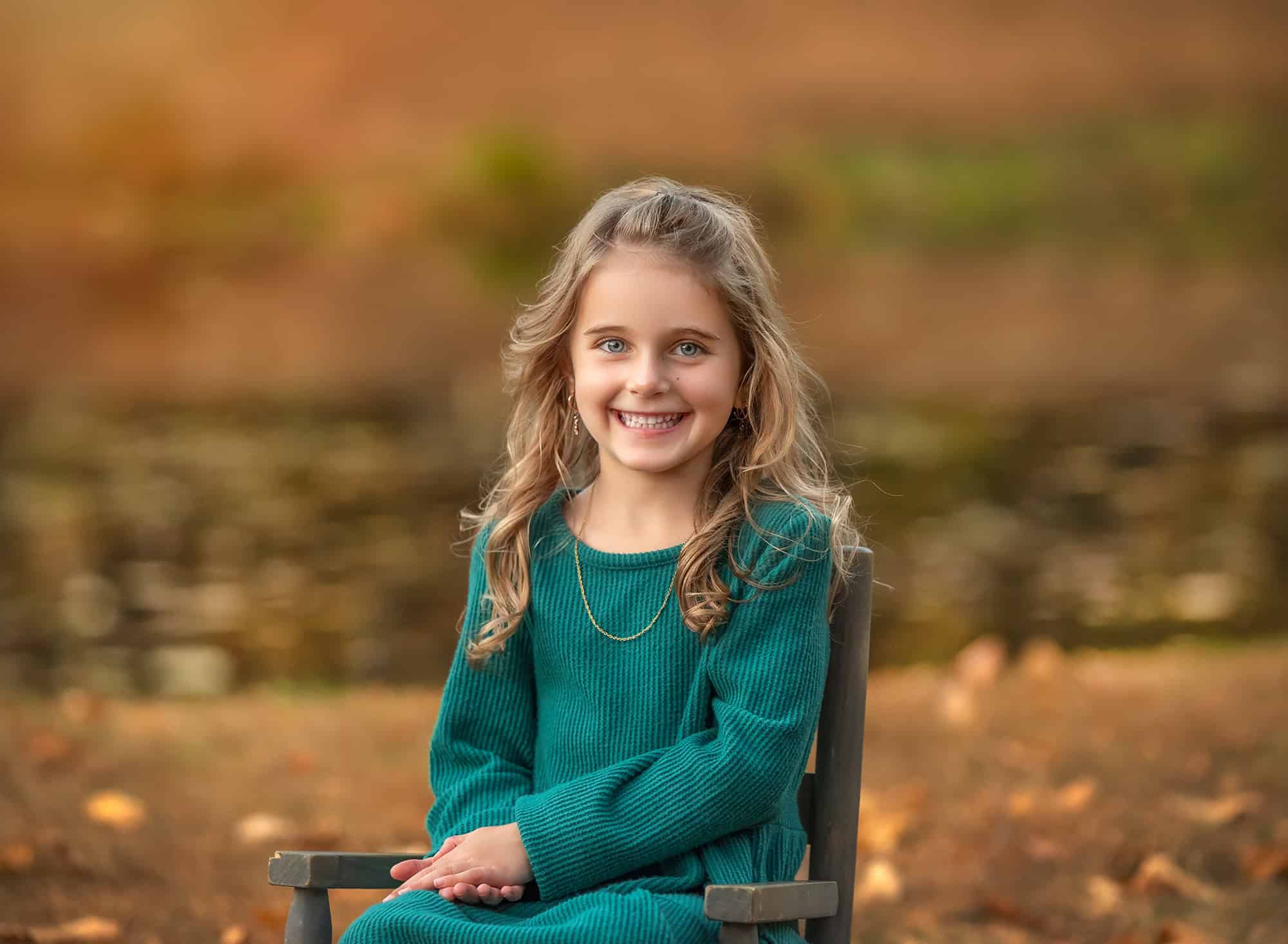 Portrait of the younger daughter on a chair near the water, gentle foliage bokeh.