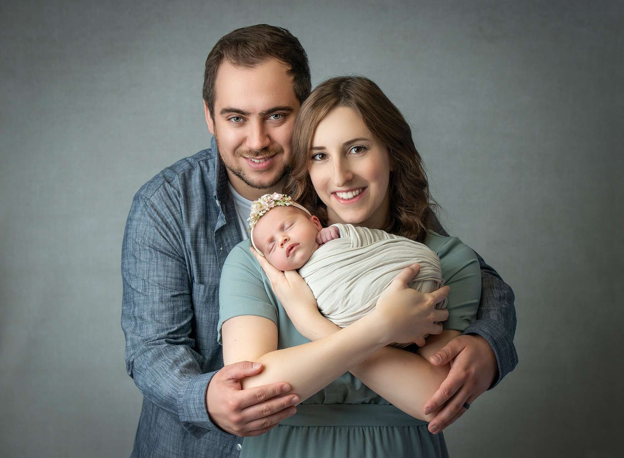 couple cradling newborn baby girl swaddled in cream