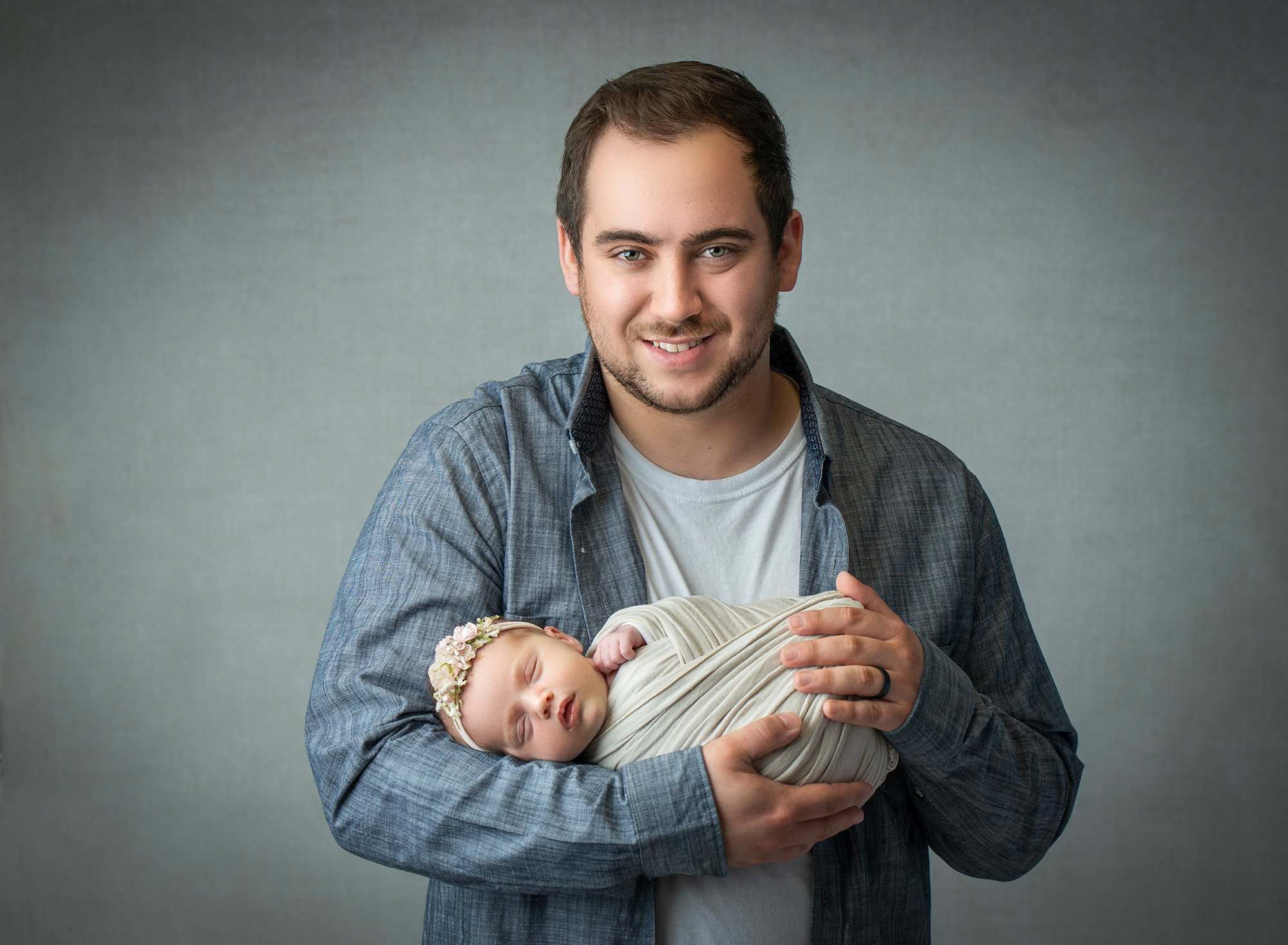dad posing while cradling newborn baby girl swaddled in cream