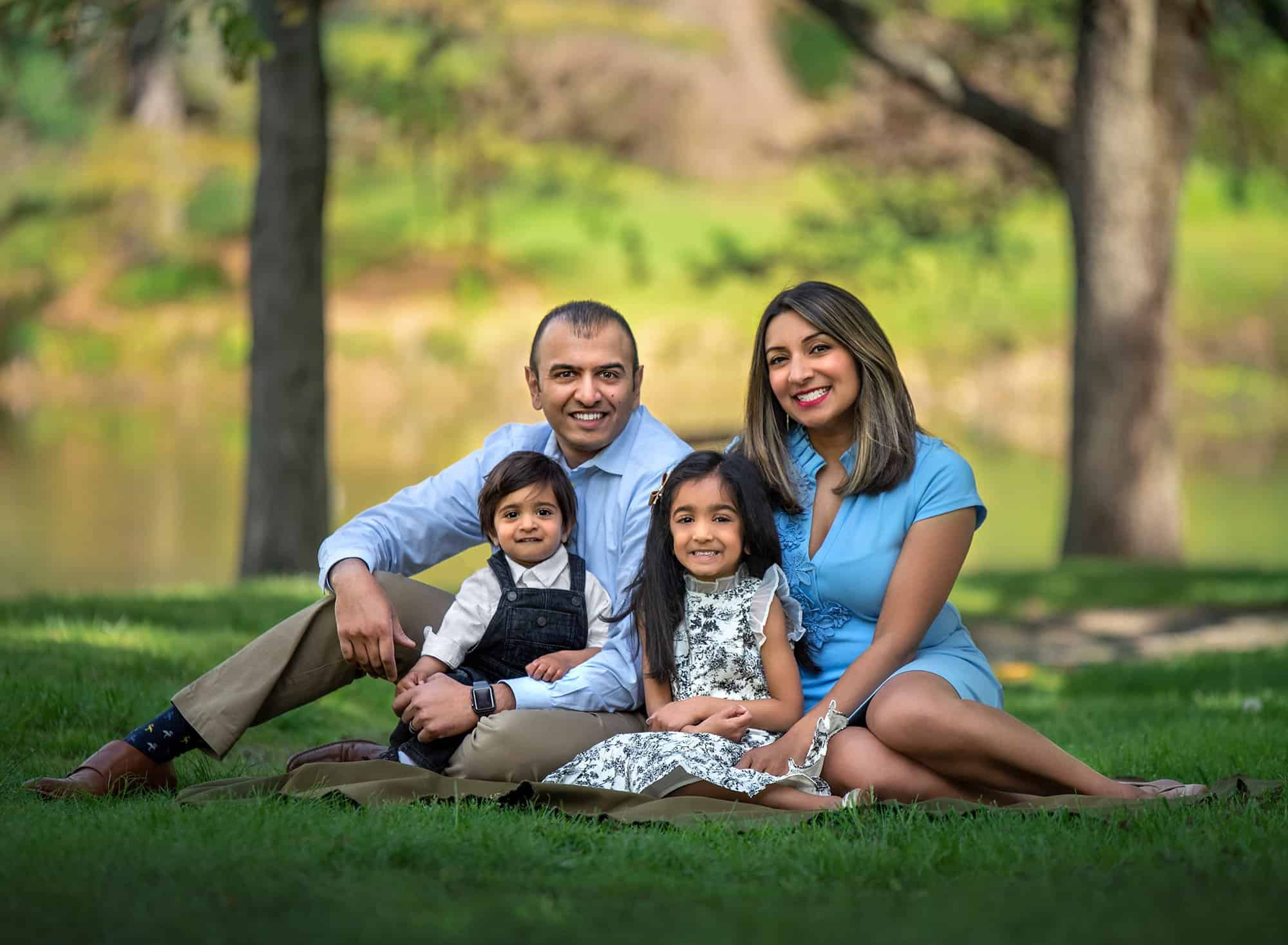 Springtime One Year Photos couple smiling sitting outside with daughter and son with trees in the background