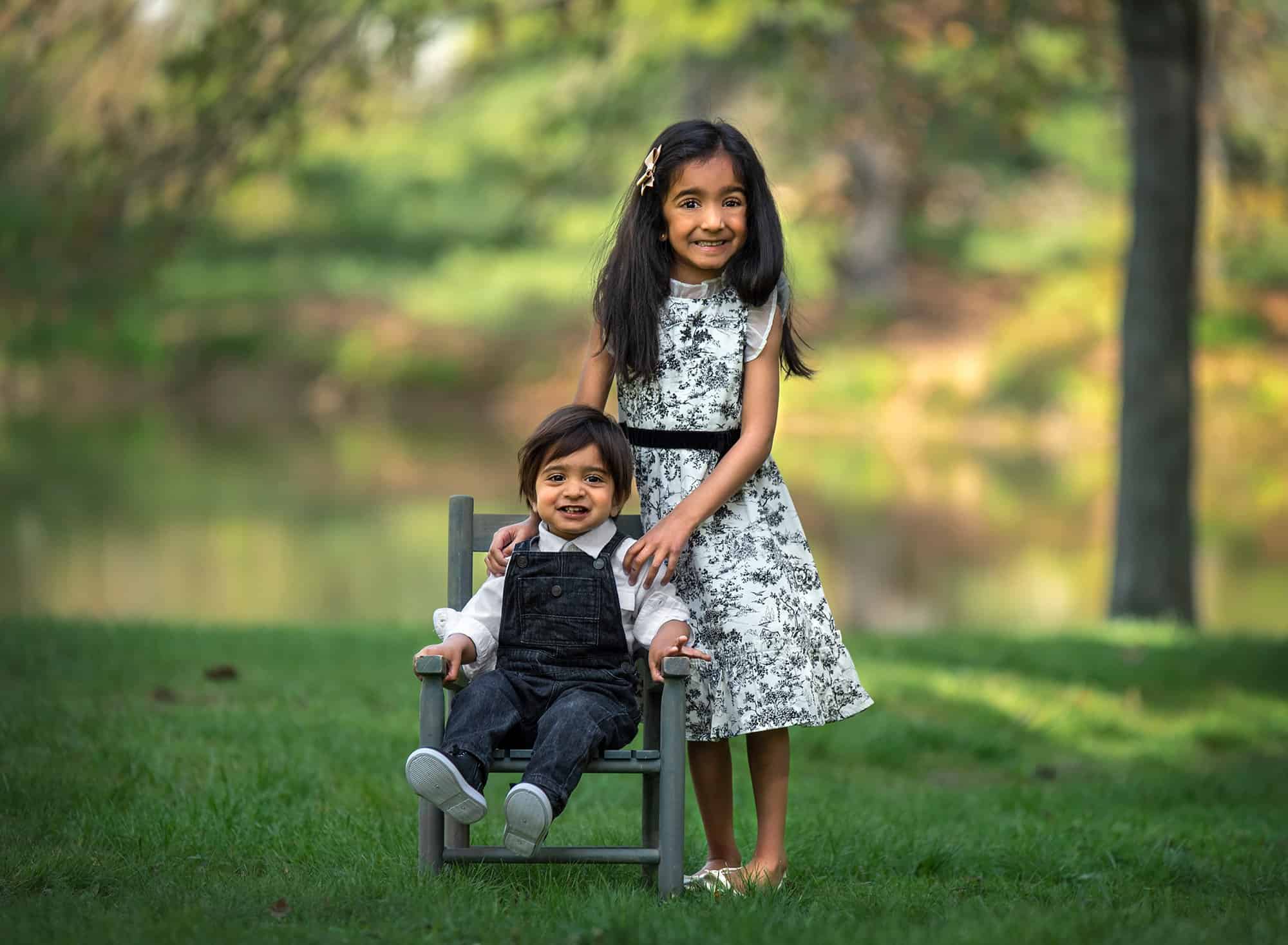 Springtime One Year Photos little girl dressed in black and white ruffled dress posing with younger brother outside as he sits in a rustic chair