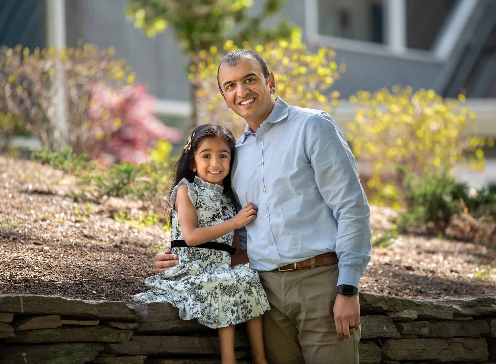 little girl smiling in her black and white dress with her arms wrapped around her father while sitting on a stone ledge