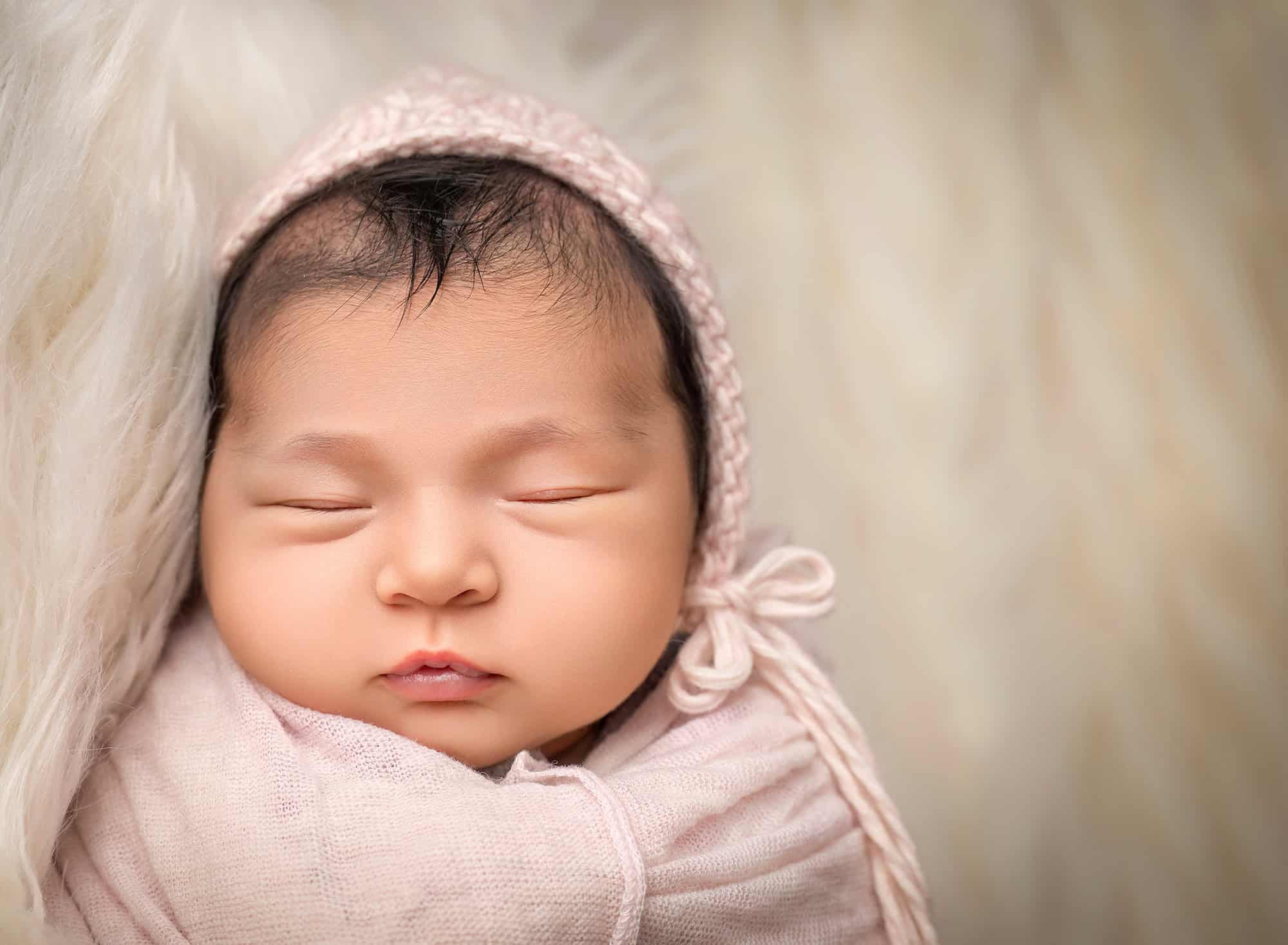 close up photo of newborn Elliana sleeping on a fur with a tiny pink bonnet