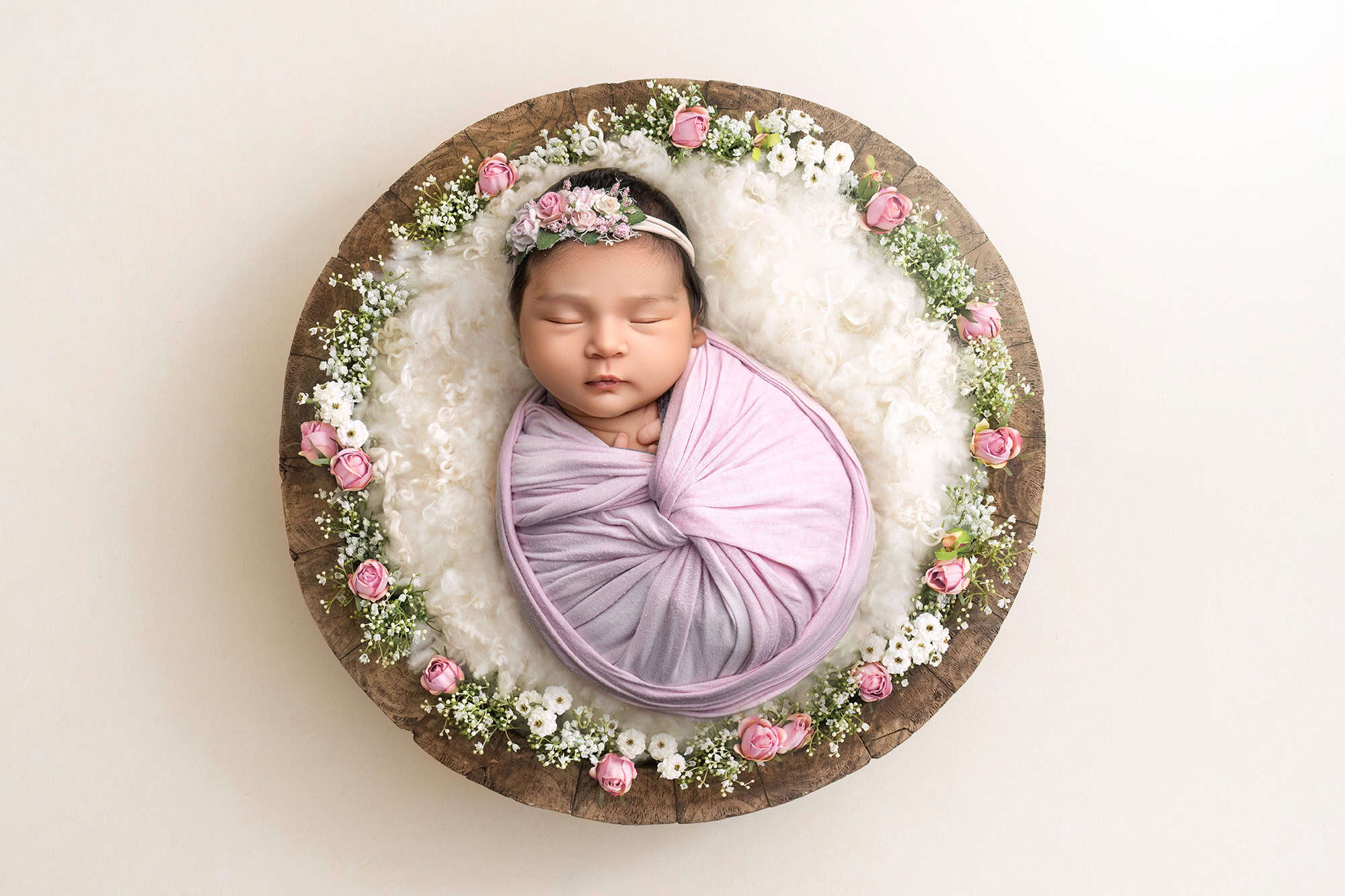 newborn baby girl wrapped in soft pink sleeping in bowl surrounded by tiny pink roses