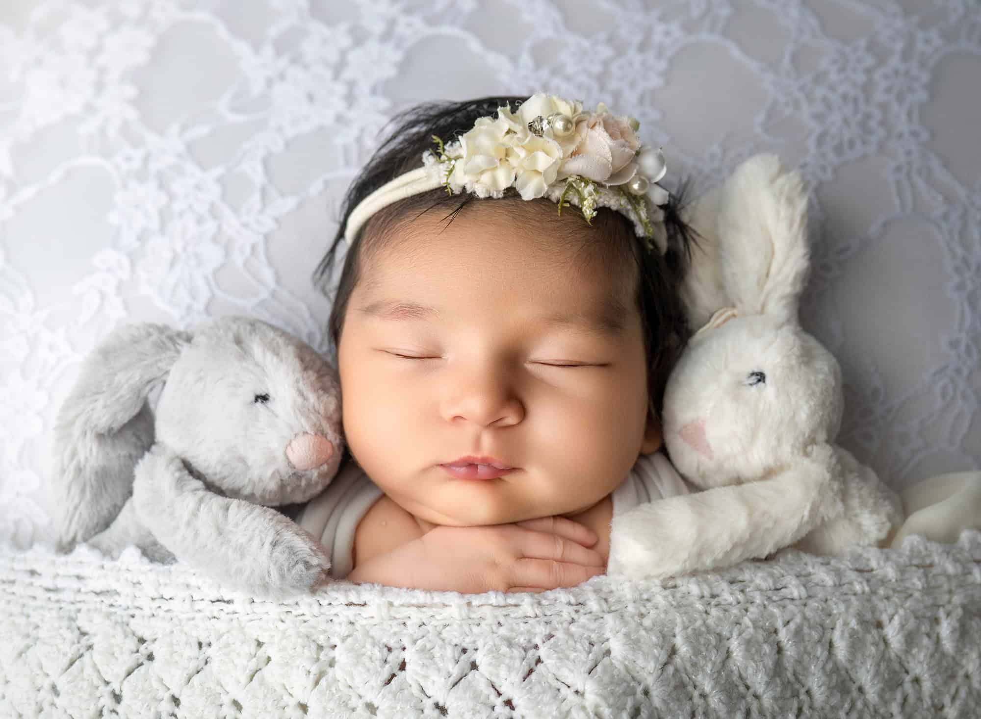 close up of newborn baby girl sleeping with 2 stuffed animals