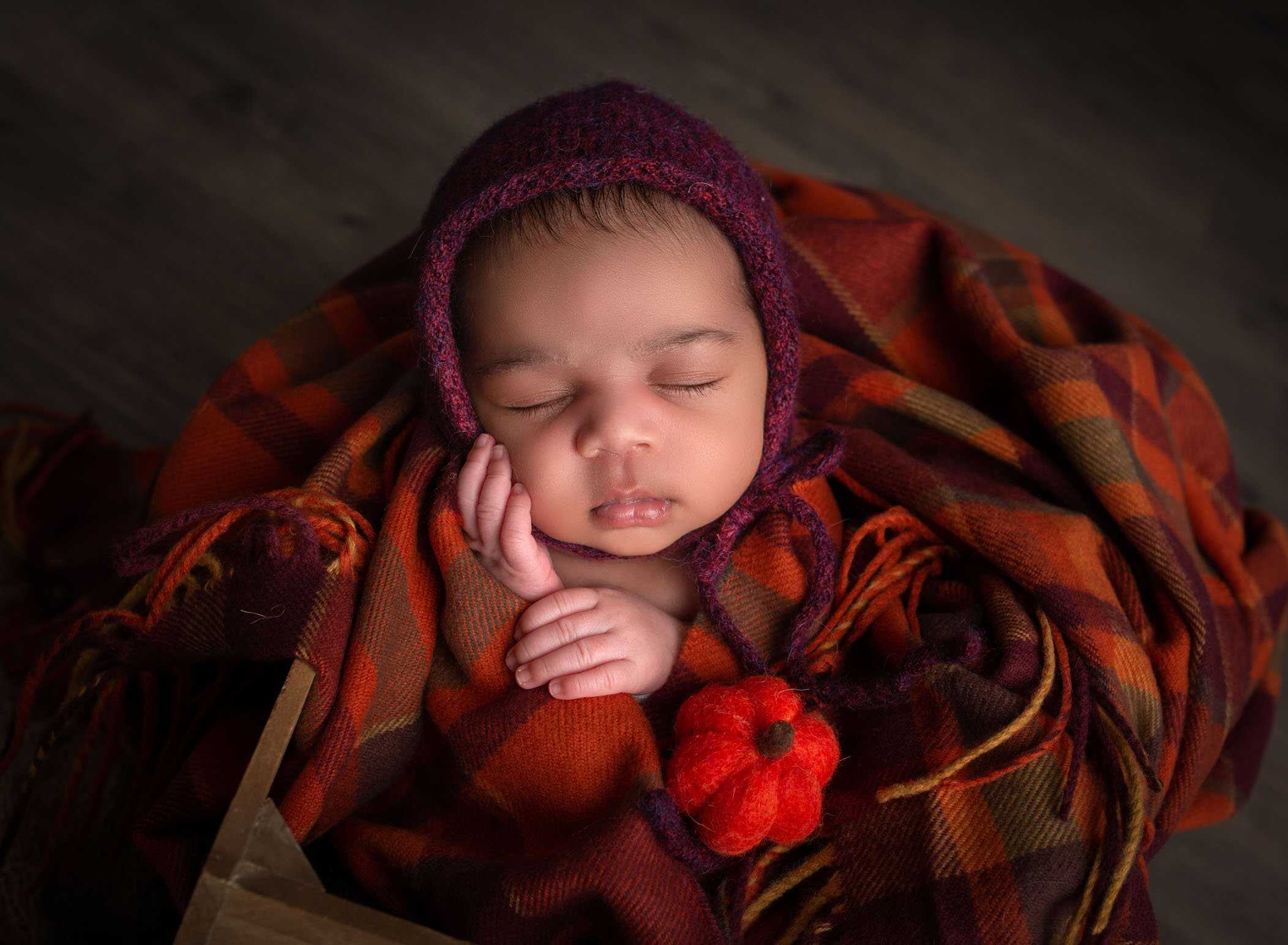 newborn wrapped in fall colors blanket sleeping with bonnet and baby pumpkin