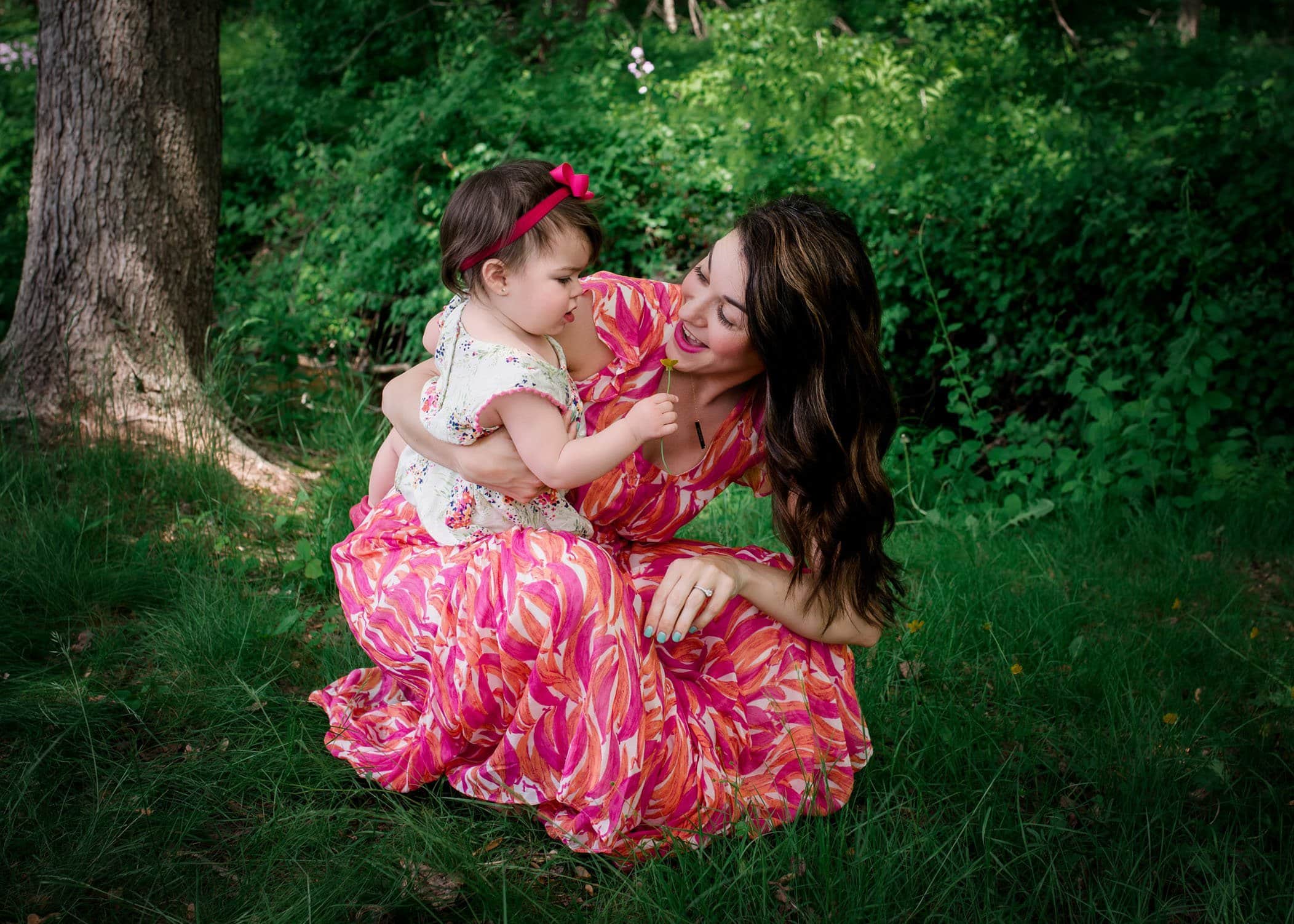 mom sitting with baby girl in the garden picking flowers