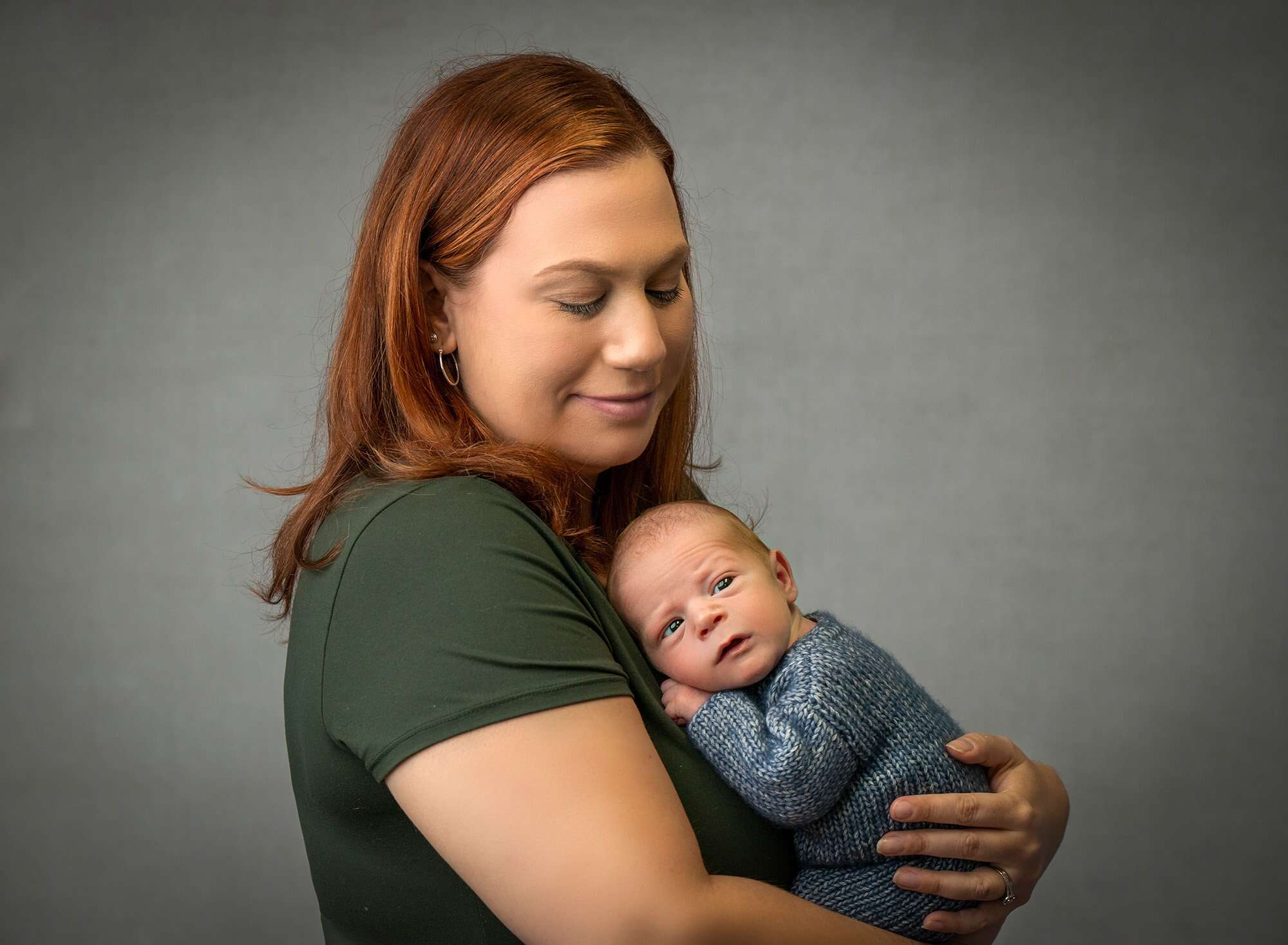mom cradling newborn baby boy in blue sweater romper