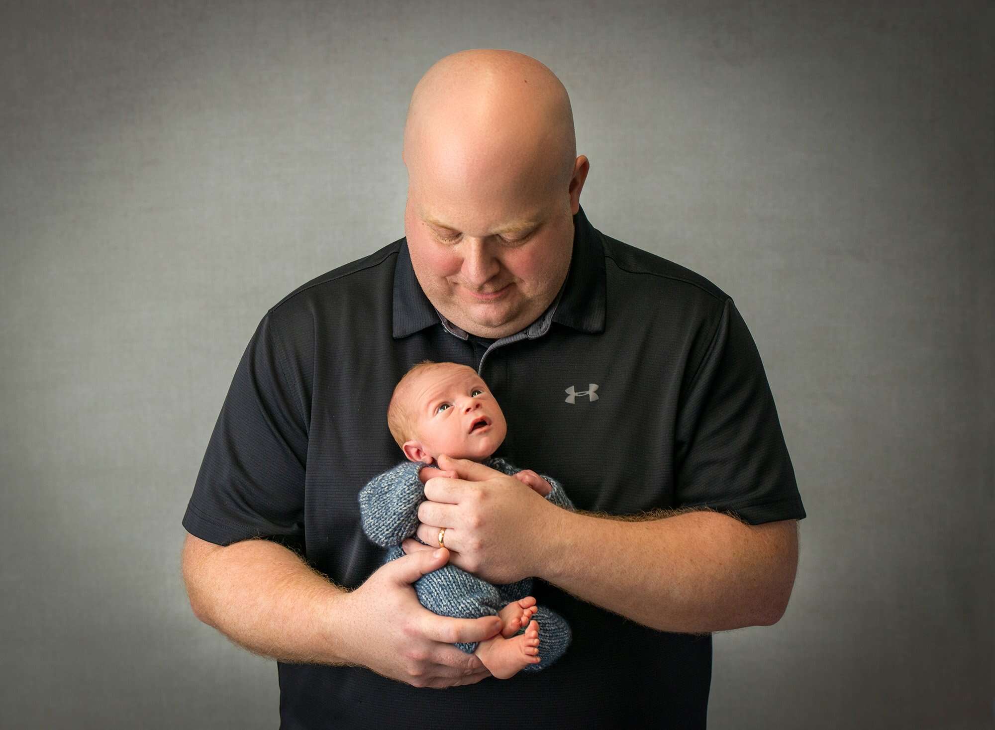 newborn baby boy in blue romper sweetly gazing up at daddy