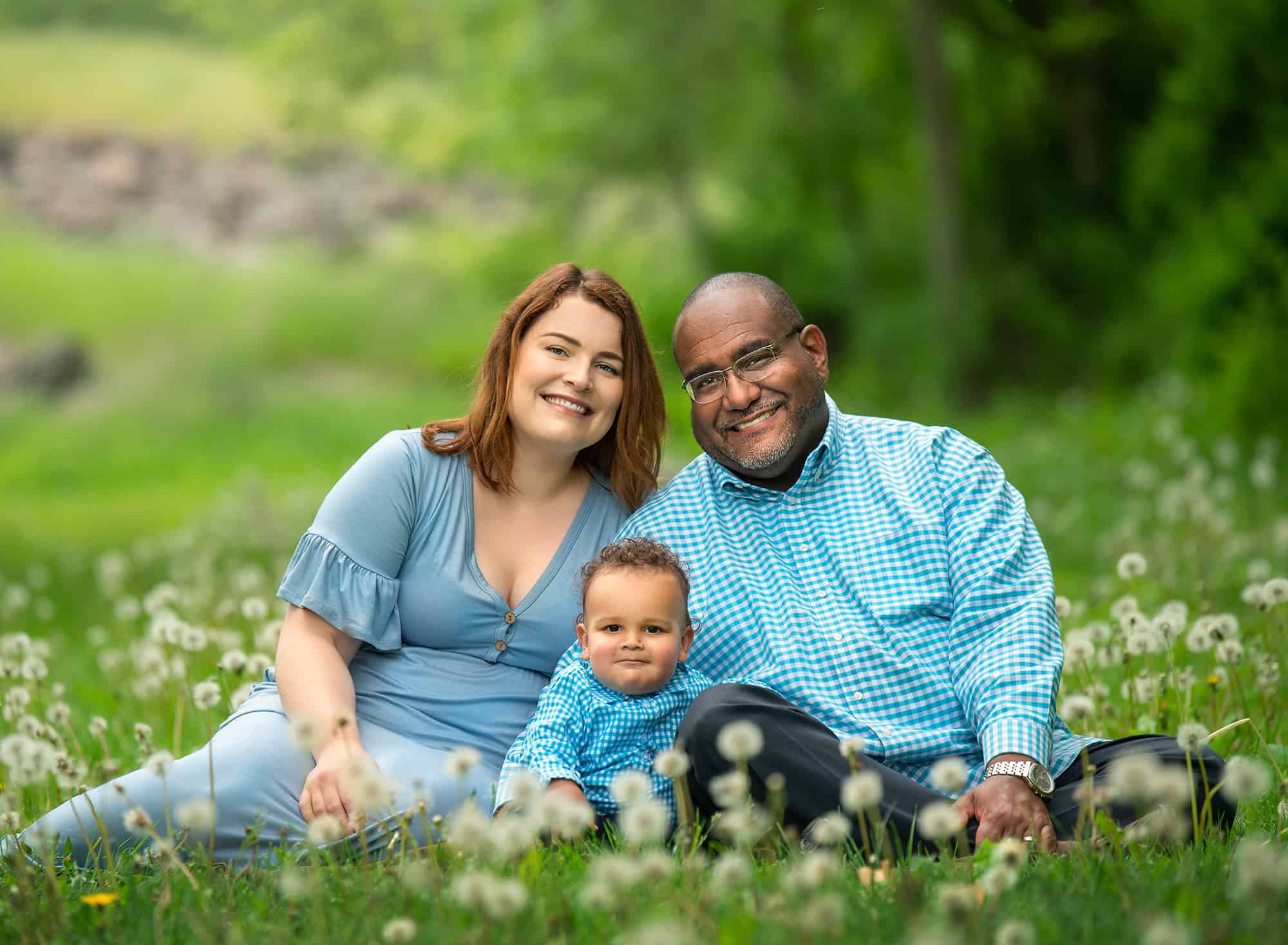 Family Photographers in CT couple sitting in dandelion field with one year old son