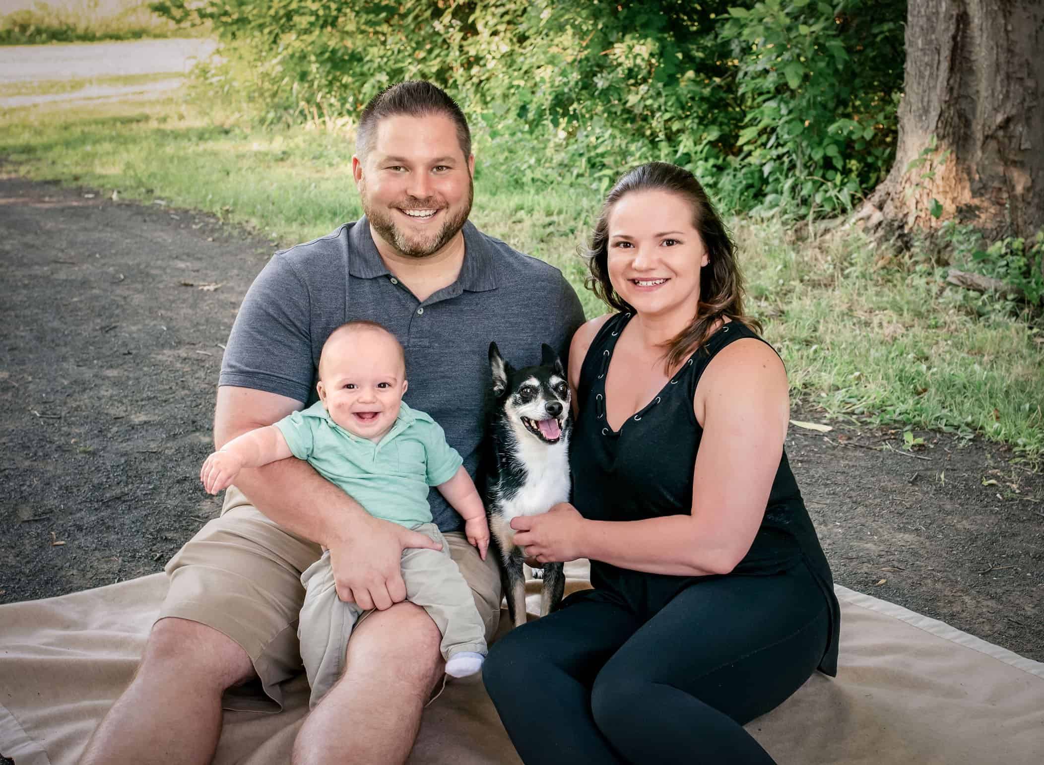 family with 6 month old boy and their dog in the park sitting on a blanket