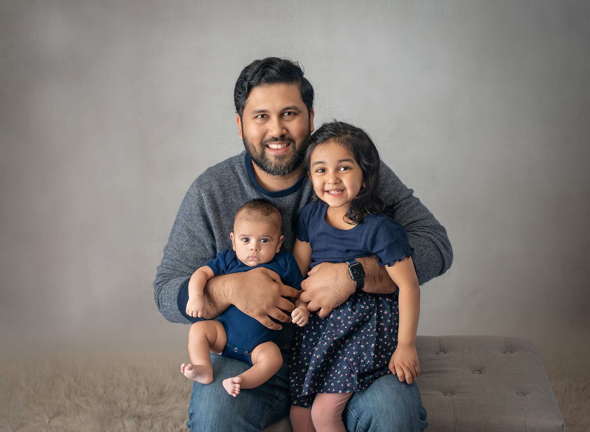 dad smiling holding young daughter and newborn baby boy all dressed in navy blue