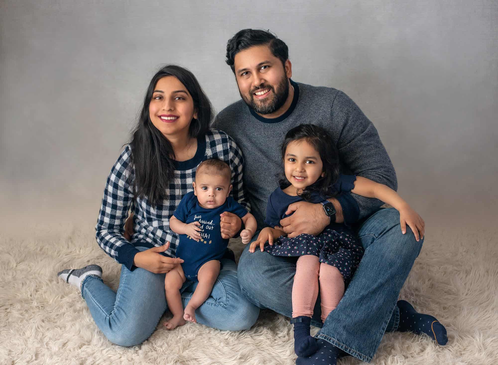 family of 4 posing together wearing navy blue on gray backdrop