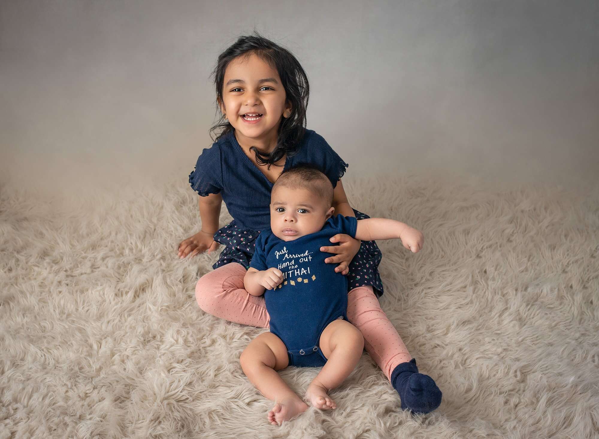 older sister holding newborn baby brother on white fluffy blanket