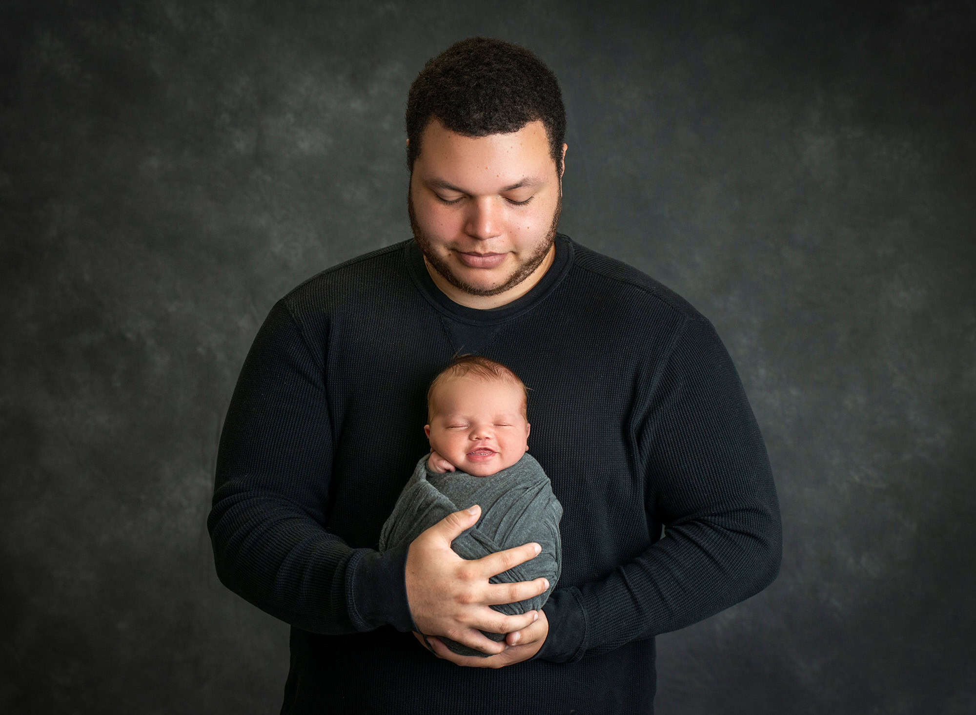 new dad looking down at newborn baby boy swaddled in blue