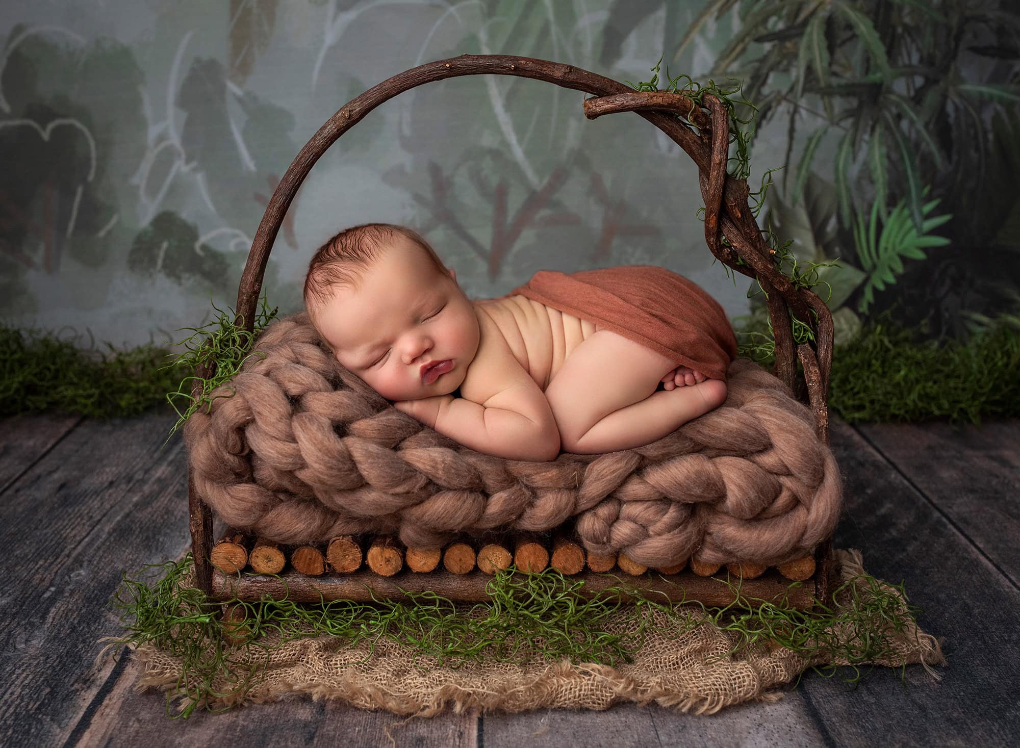 newborn baby boy asleep on wooden bed draped in orange