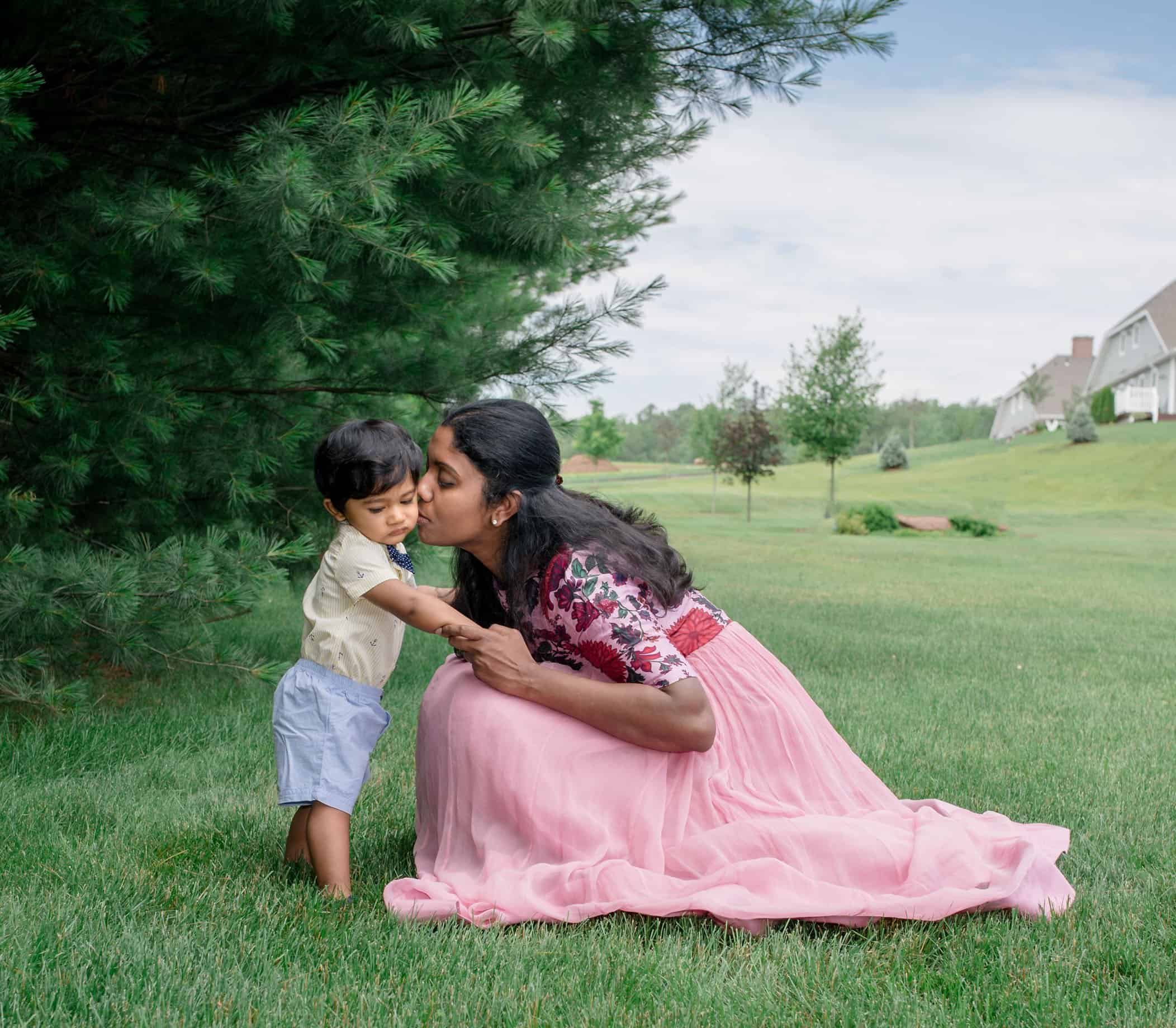 Mom kissing her 8 mo old boy on the cheek in the garden