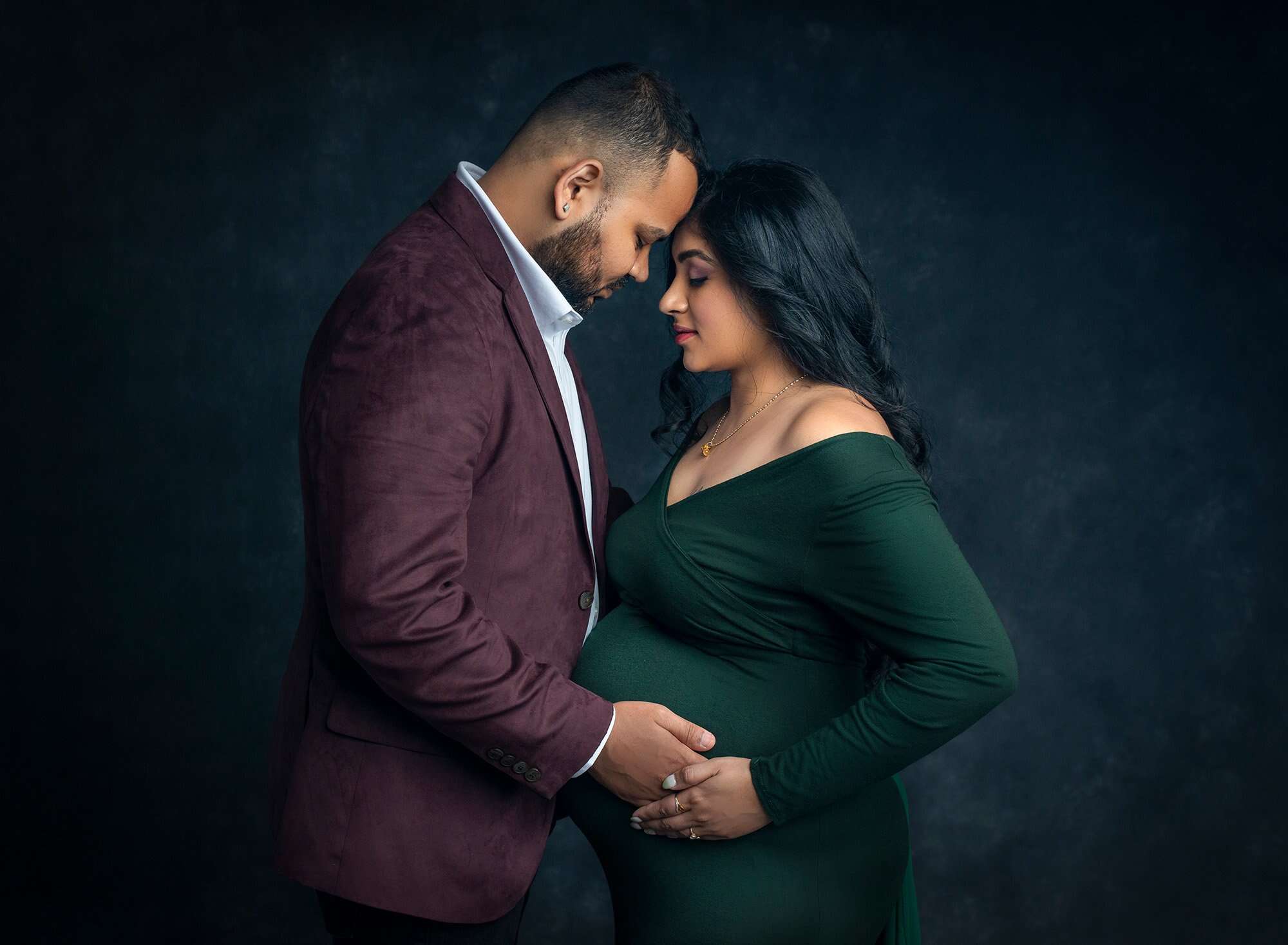 pregnant woman wearing green dress holding partners hand on pregnant stomach