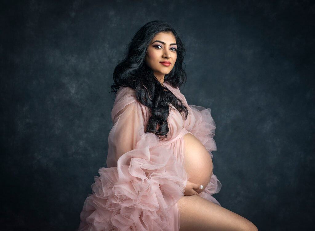 Indian Goddess Maternity photographs pregnant woman posing wearing ruffled pink dress exposing pregnant stomach