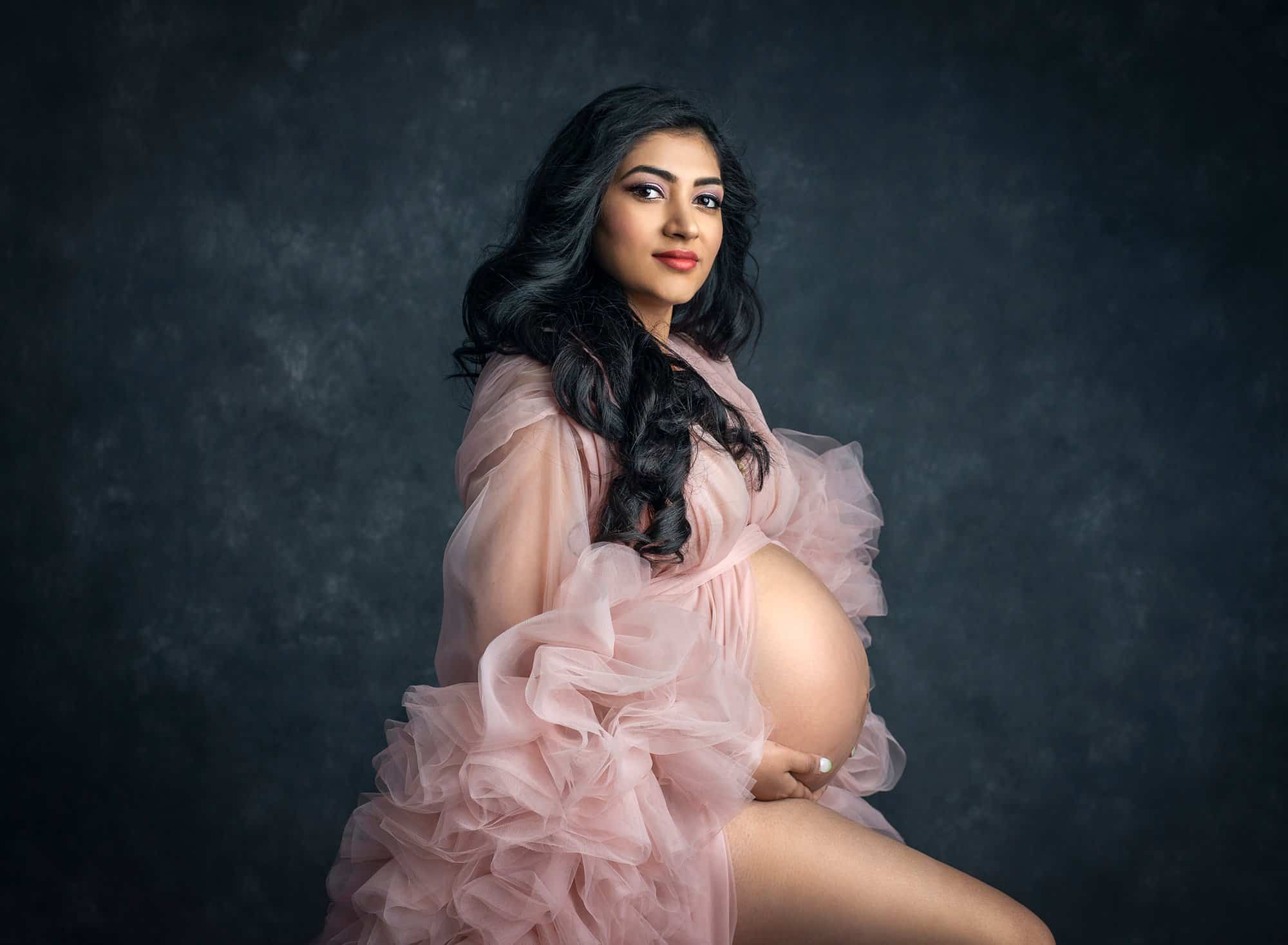 Indian Goddess Maternity photographs pregnant woman posing wearing ruffled pink dress exposing pregnant stomach