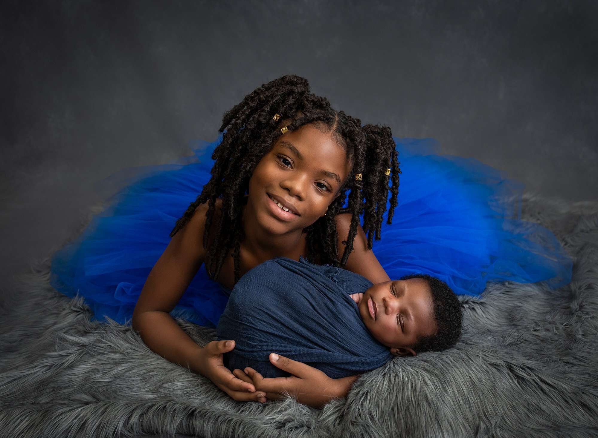 Jamaican boy newborn photographs older sister wearing blue dress cradling newborn baby brother swaddled in blue
