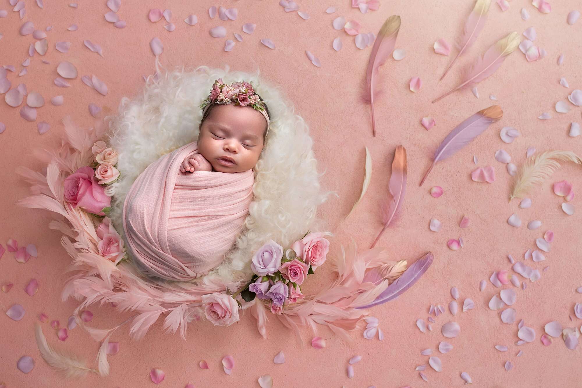 girly girl newborn photos newborn baby girl swaddled in pink sleeping on fuzzy blanket surrounded by feathers and flower petals
