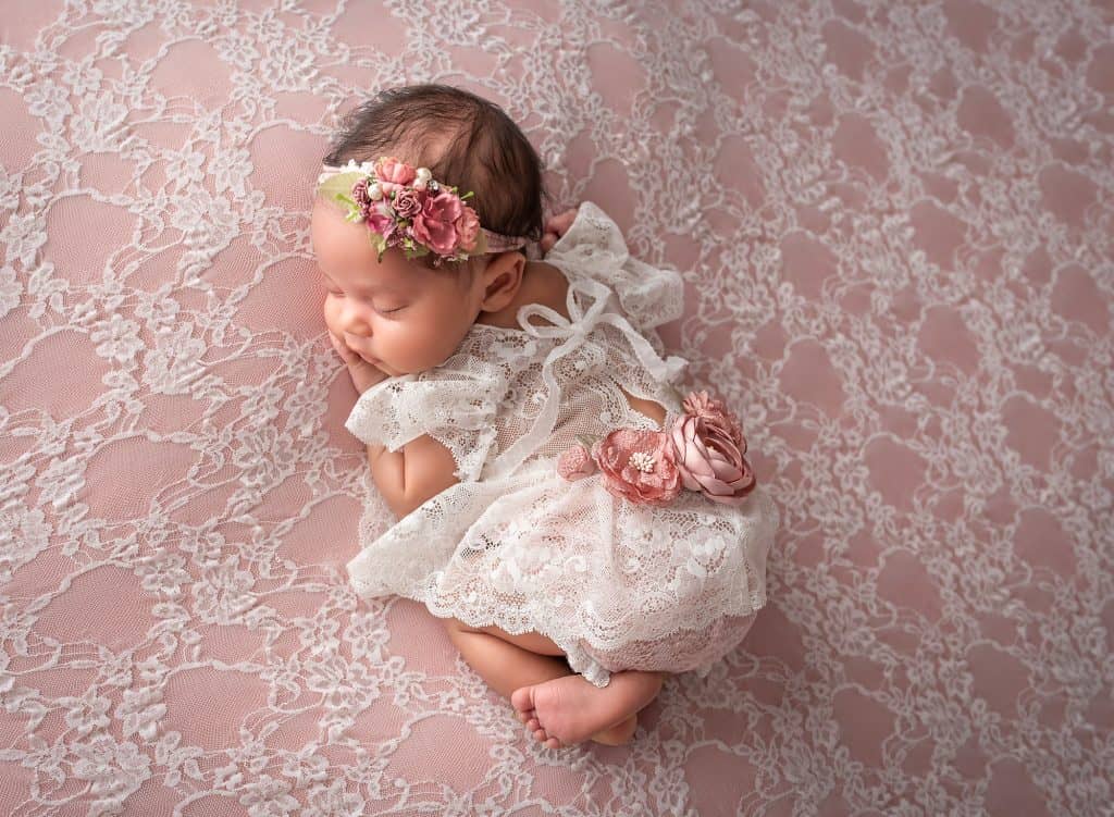 newborn baby girl laying on stomach on top of pink lace wearing lace dress and pink floral headband
