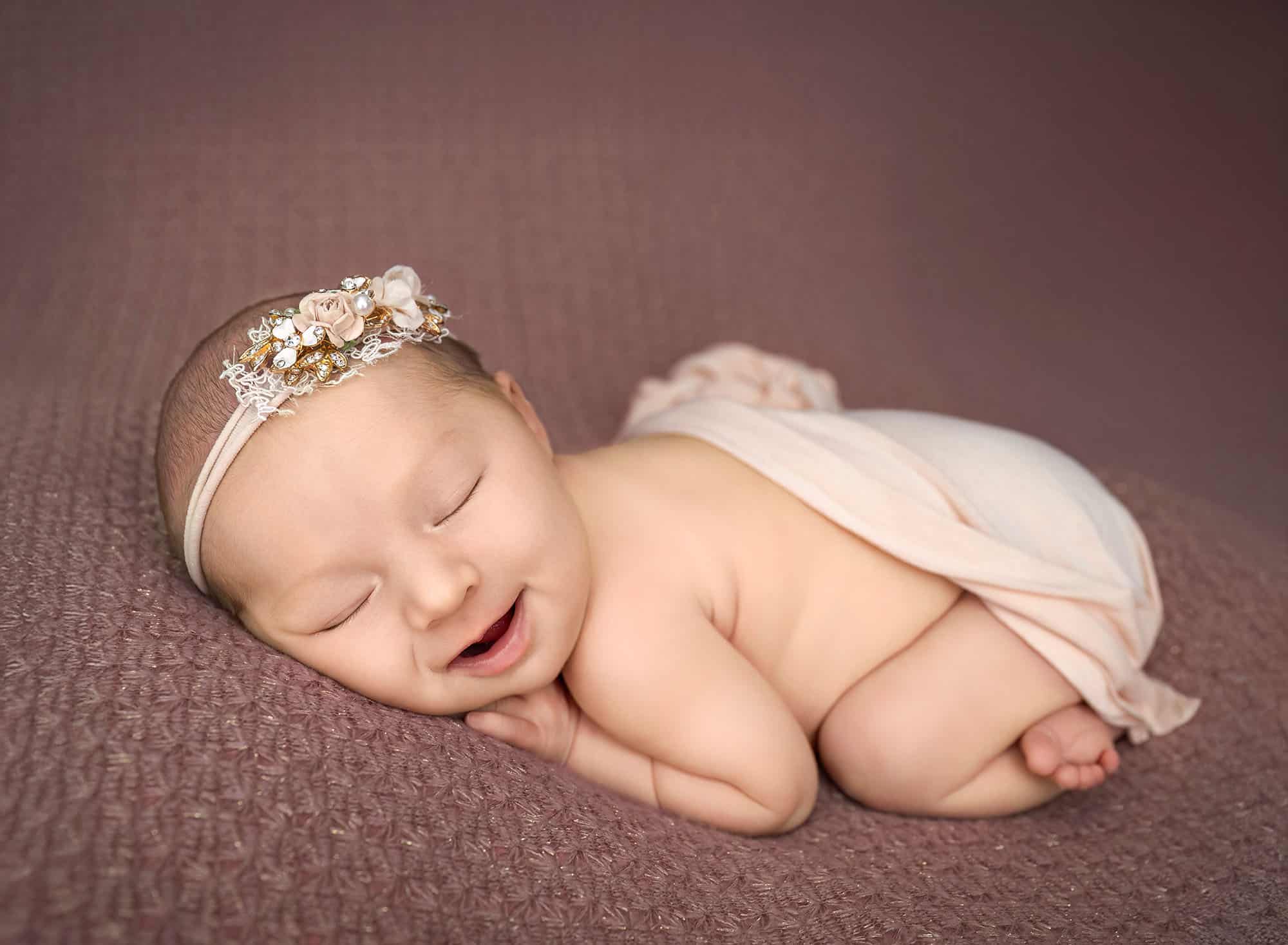 Newborn girl smiling in wrap—results of preparing siblings for newborn photos calmly