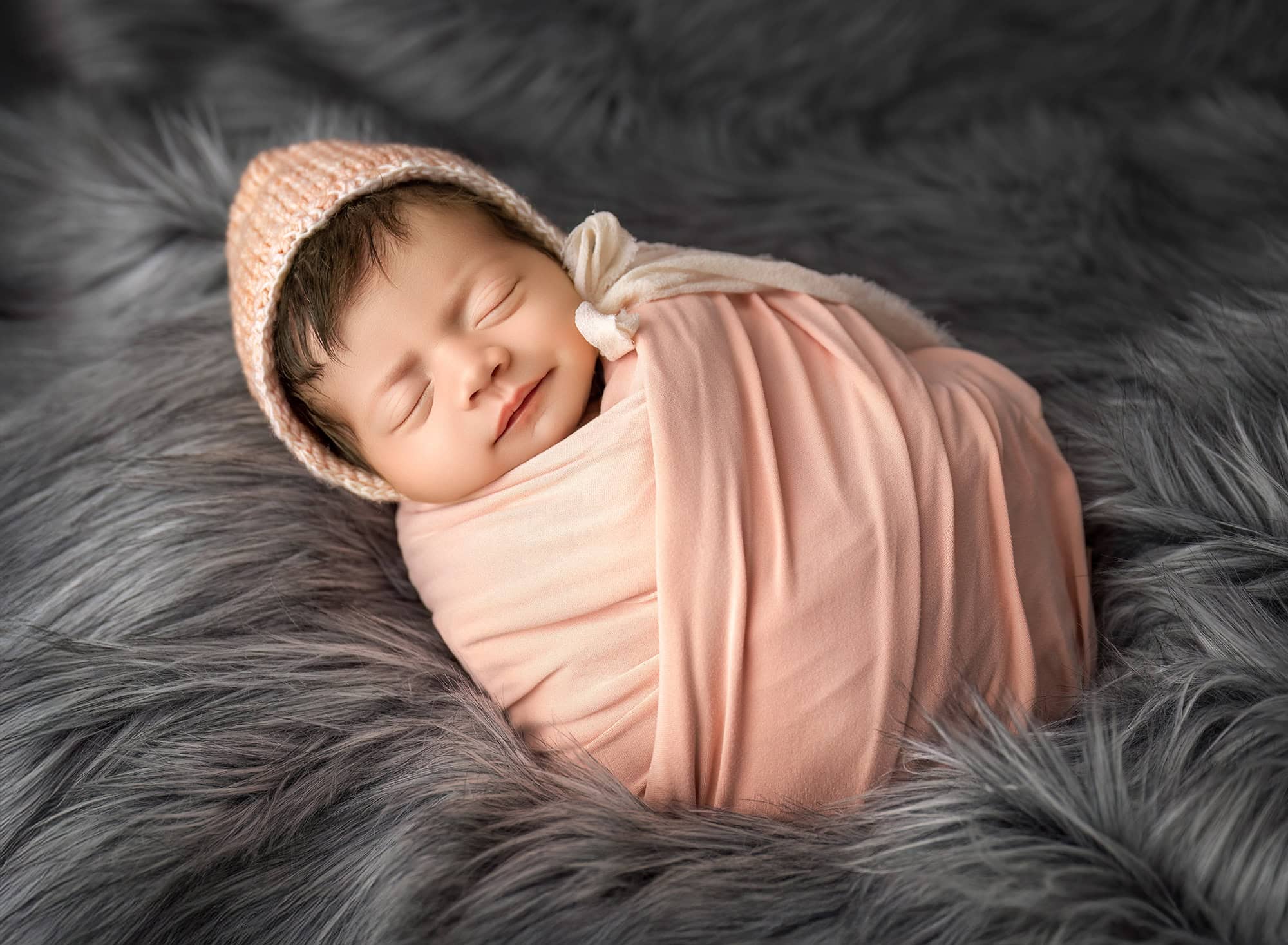 Sleeping baby wrapped in peach fabric with gentle folds on a neutral backdrop.
