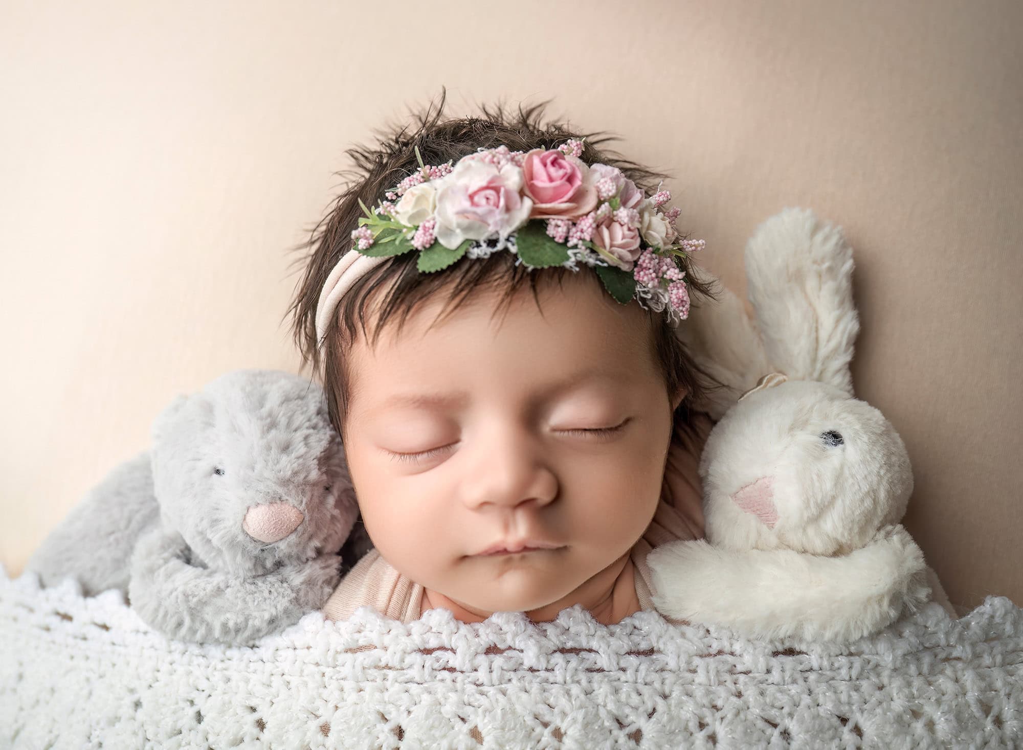 Close-up of Lee Anne with floral headband, resting between two plush toys.