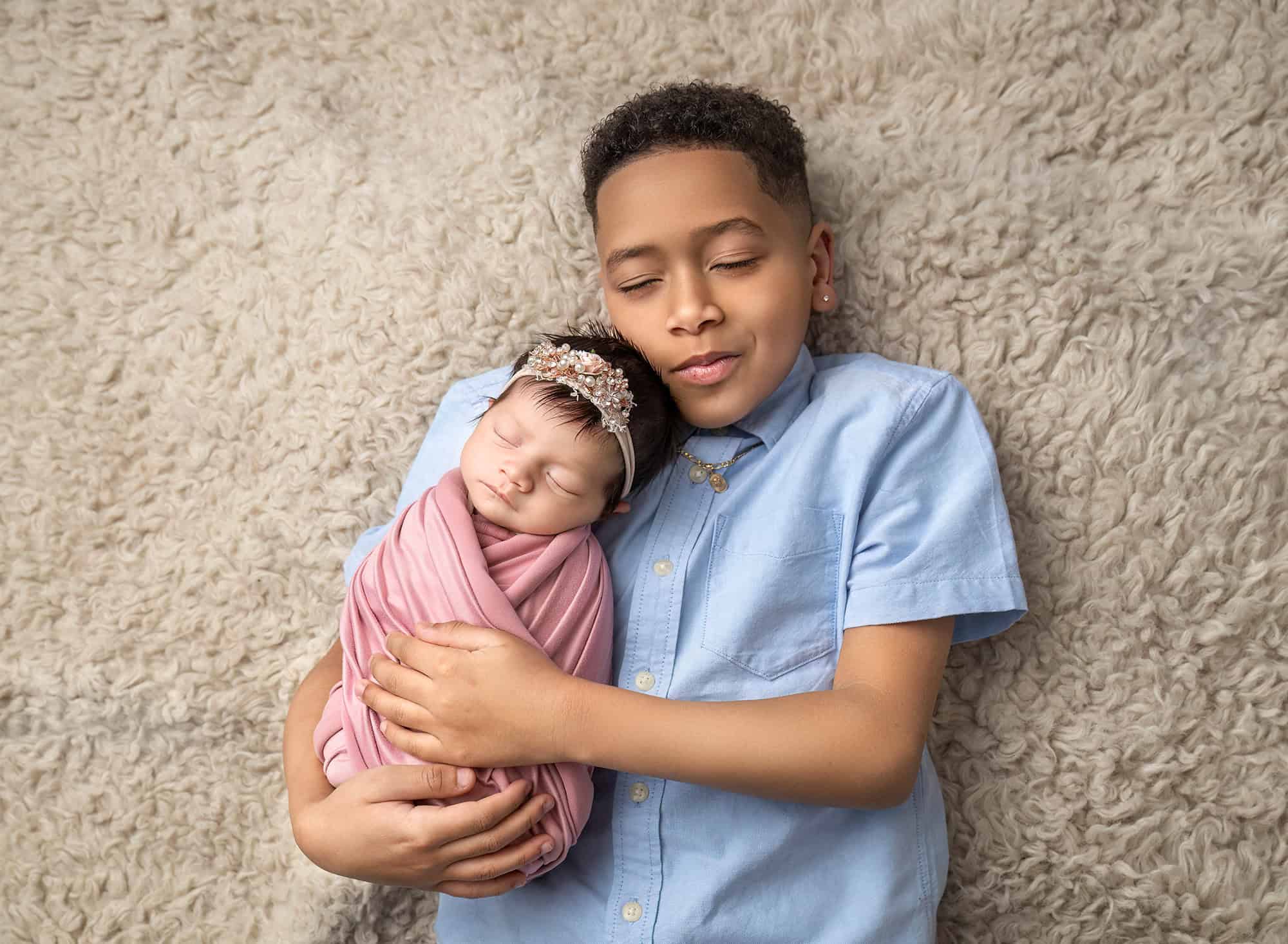 Ten-year-old brother Joseph cuddling newborn sister on a cozy rug.