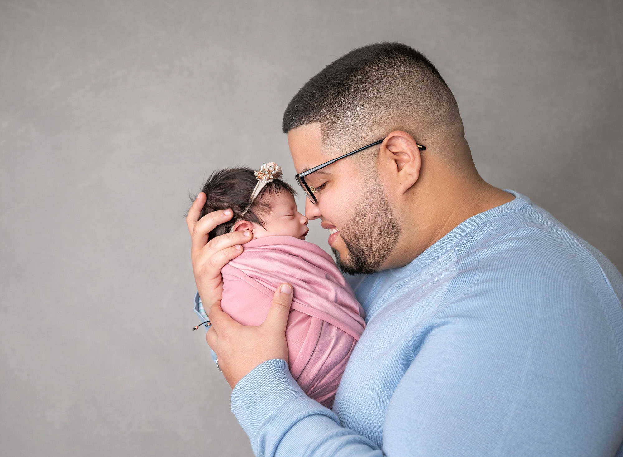 Father forehead to newborn, both smiling softly.