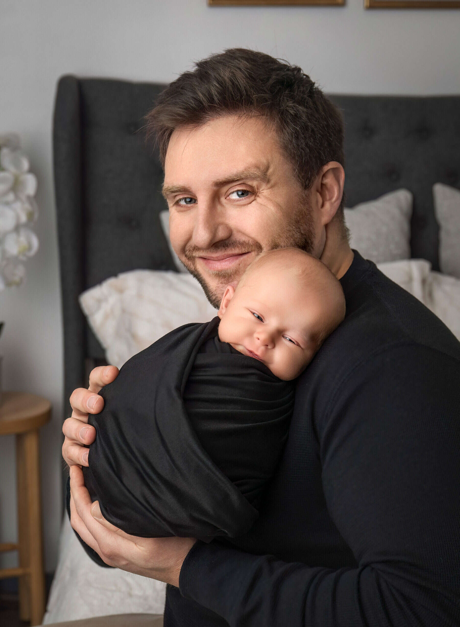 Dad holding newborn on his shoulder with both of them smiling.