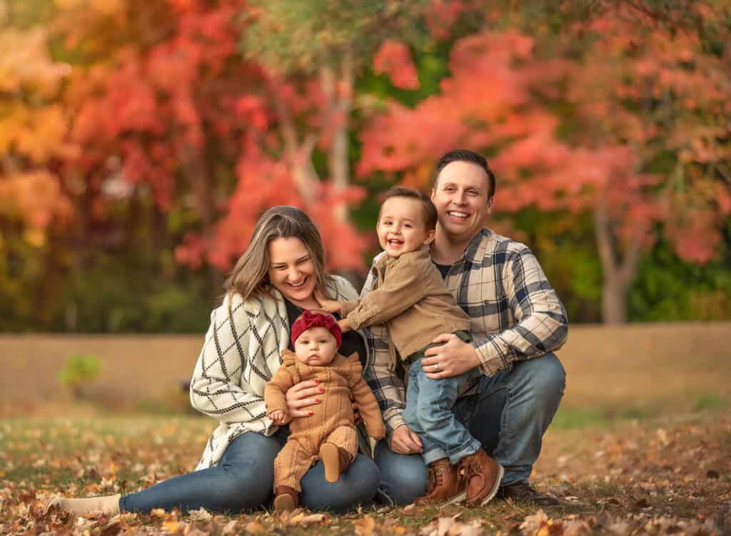 Family cuddling on a blanket under rich autumn leaves.