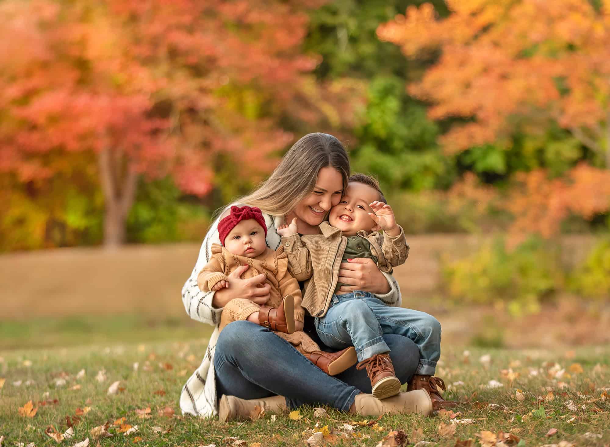Mom hugging Lincoln while holding Kennedy among colorful trees.