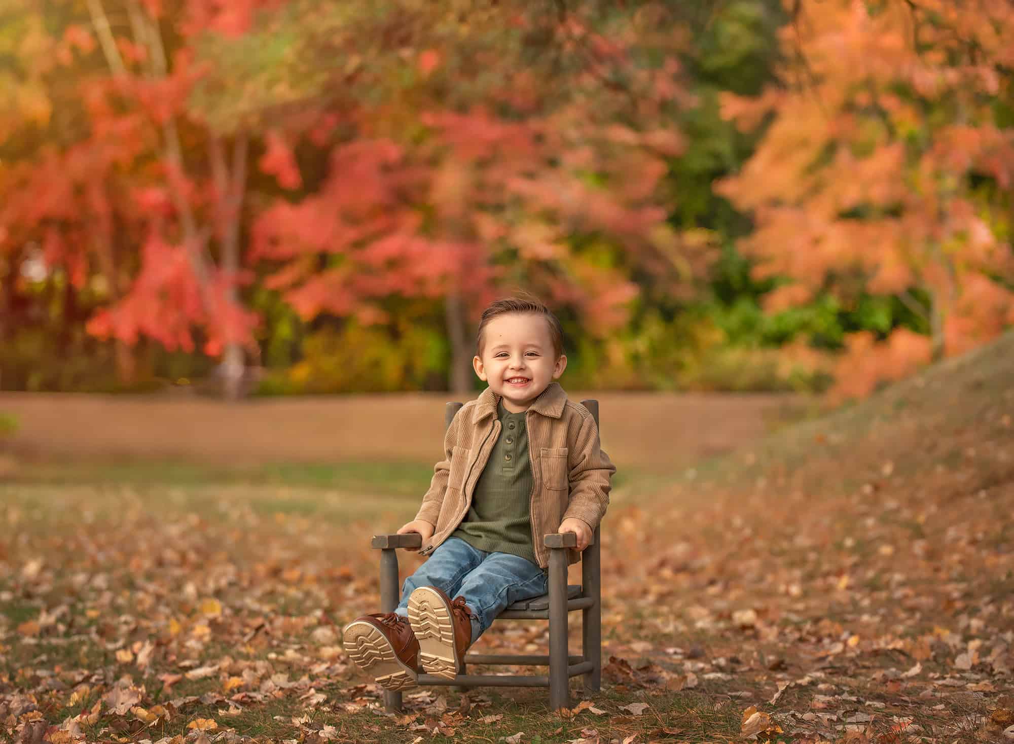 Lincoln grinning on a small chair with orange foliage behind him.
