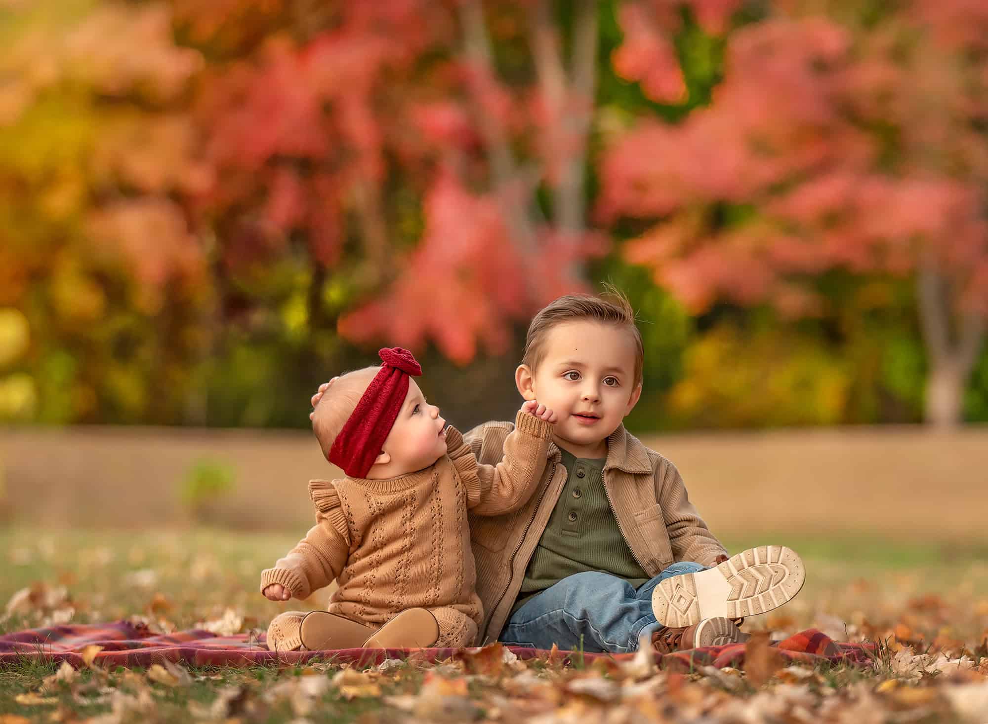 Siblings on a plaid blanket; baby Kennedy reaching toward Lincoln.
