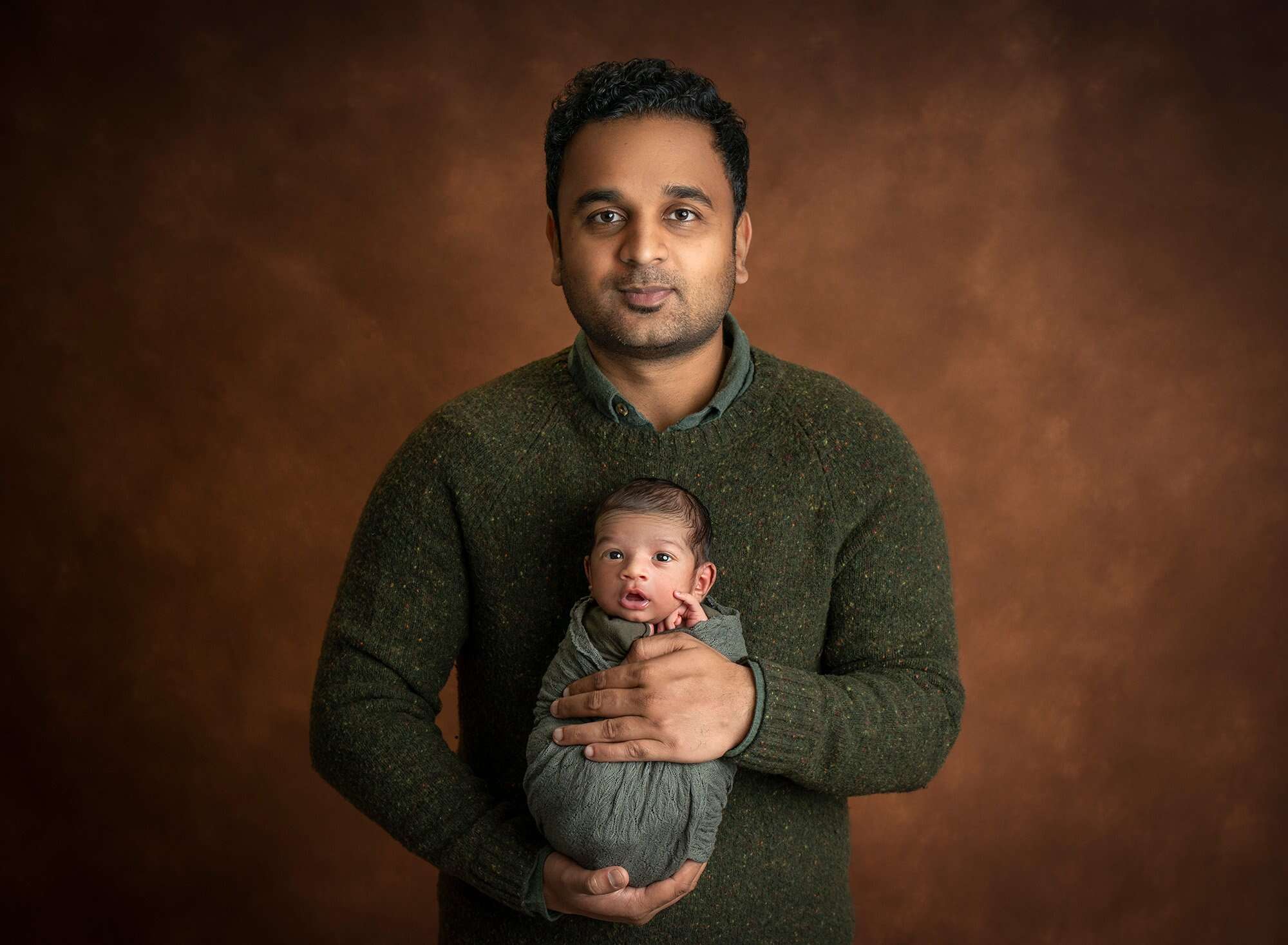 new dad cradling awake newborn baby boy swaddled in green