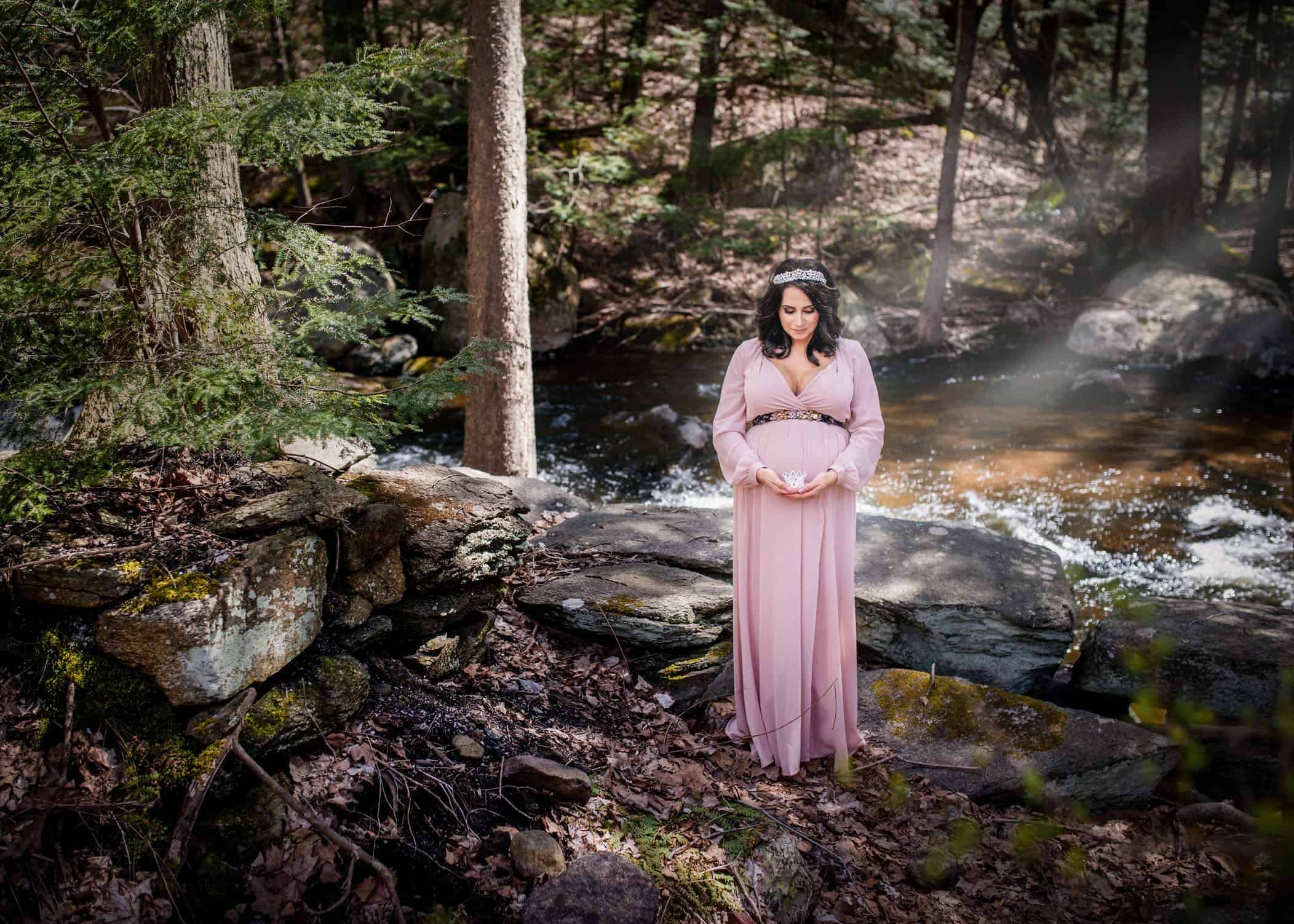 pregnant woman in pink dress wearing a tiara and holding a newborn crown in front of her belly