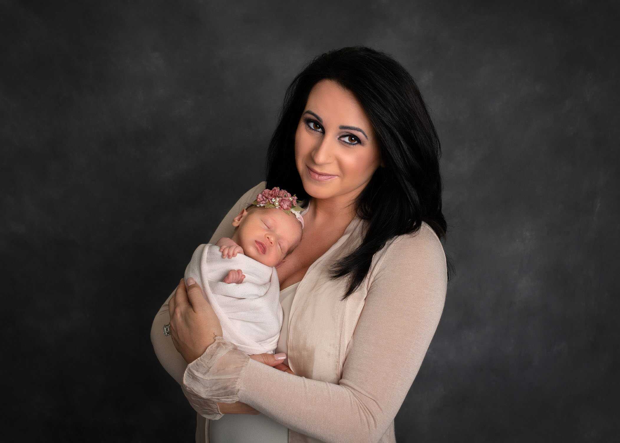 mom holding her newborn daughter on her chest and smiling at the camera