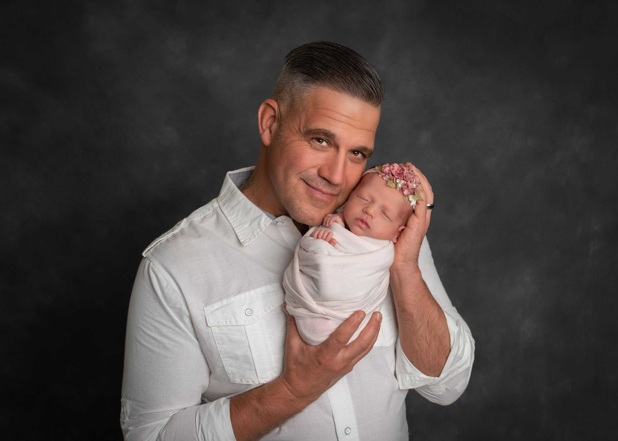 Dad holding his newborn daughter in his hands cheek to cheek