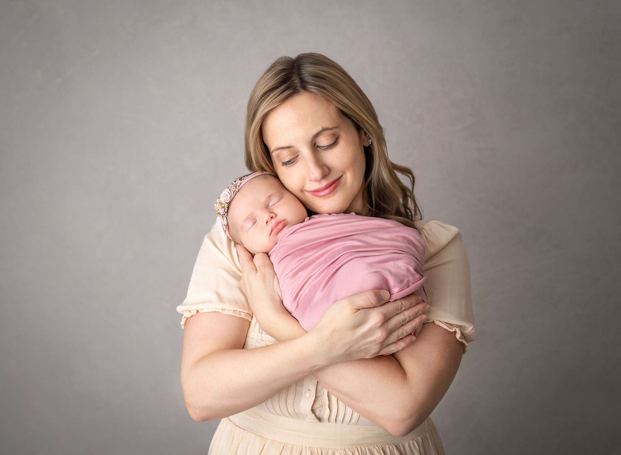 Mother holding newborn close — Mom in cream dress cradles Mia wrapped in blush.