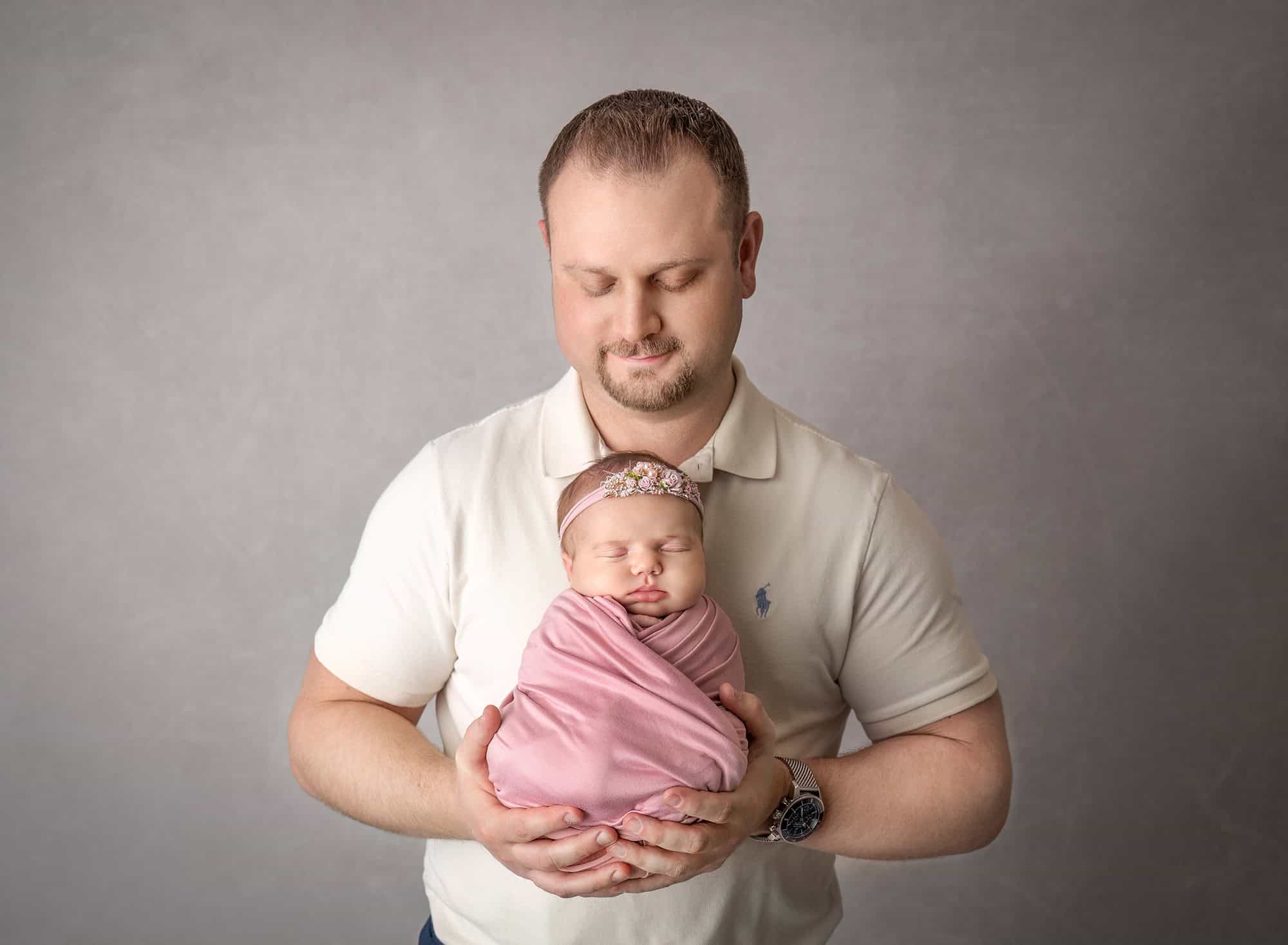 Father with newborn — Dad’s hands support sleeping baby in rose wrap.