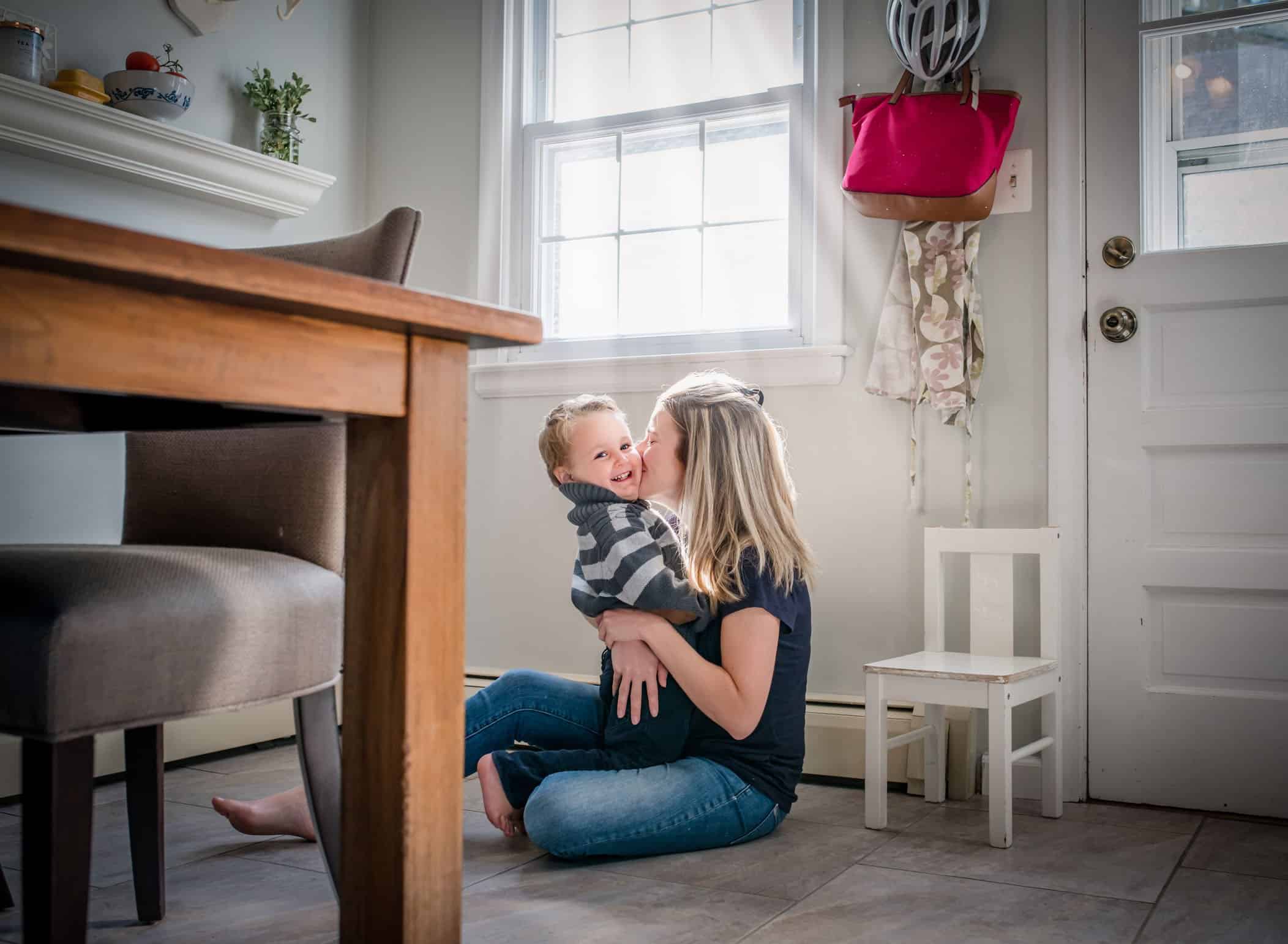 Mom kissing toddler son on cheek on kitchen floor